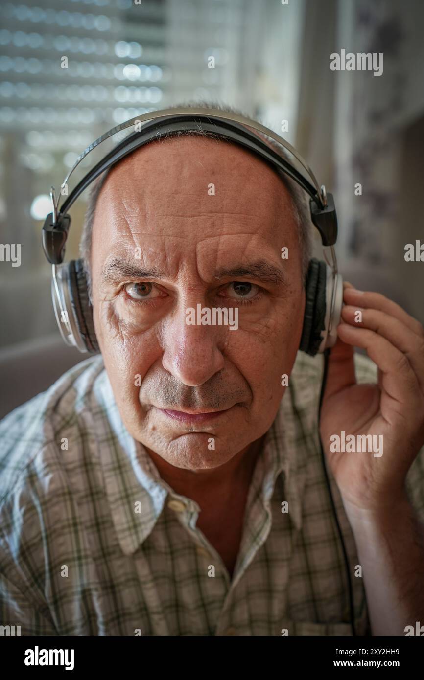 Deutschland. August 2024. Mann mit Kopfhörern hört Musik oder Hörbücher auf dem Sofa Stockfoto