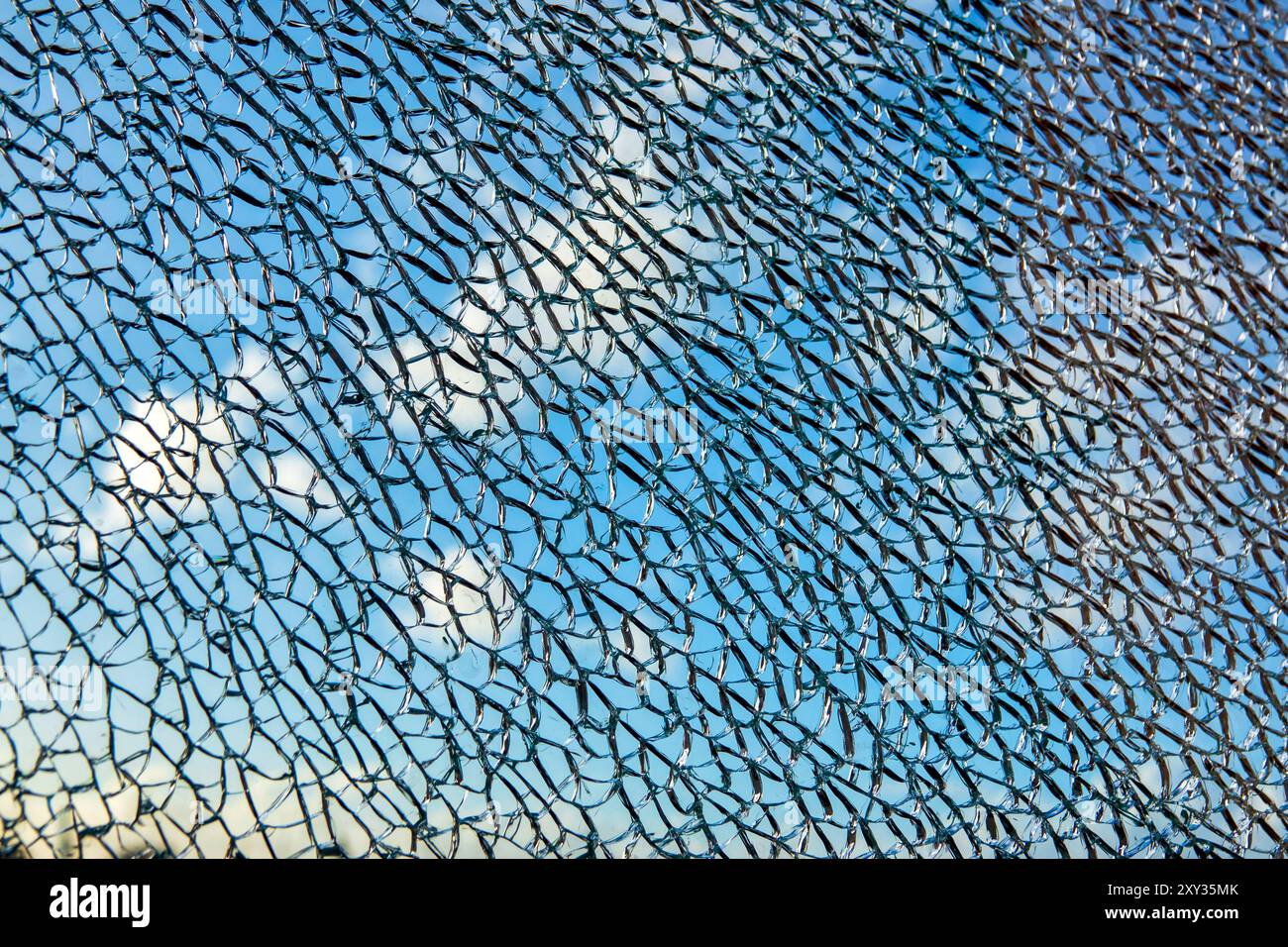 Eine Nahaufnahme einer zerrissenen Glasoberfläche vor einem Hintergrund von blauem Himmel und Wolken. Stockfoto