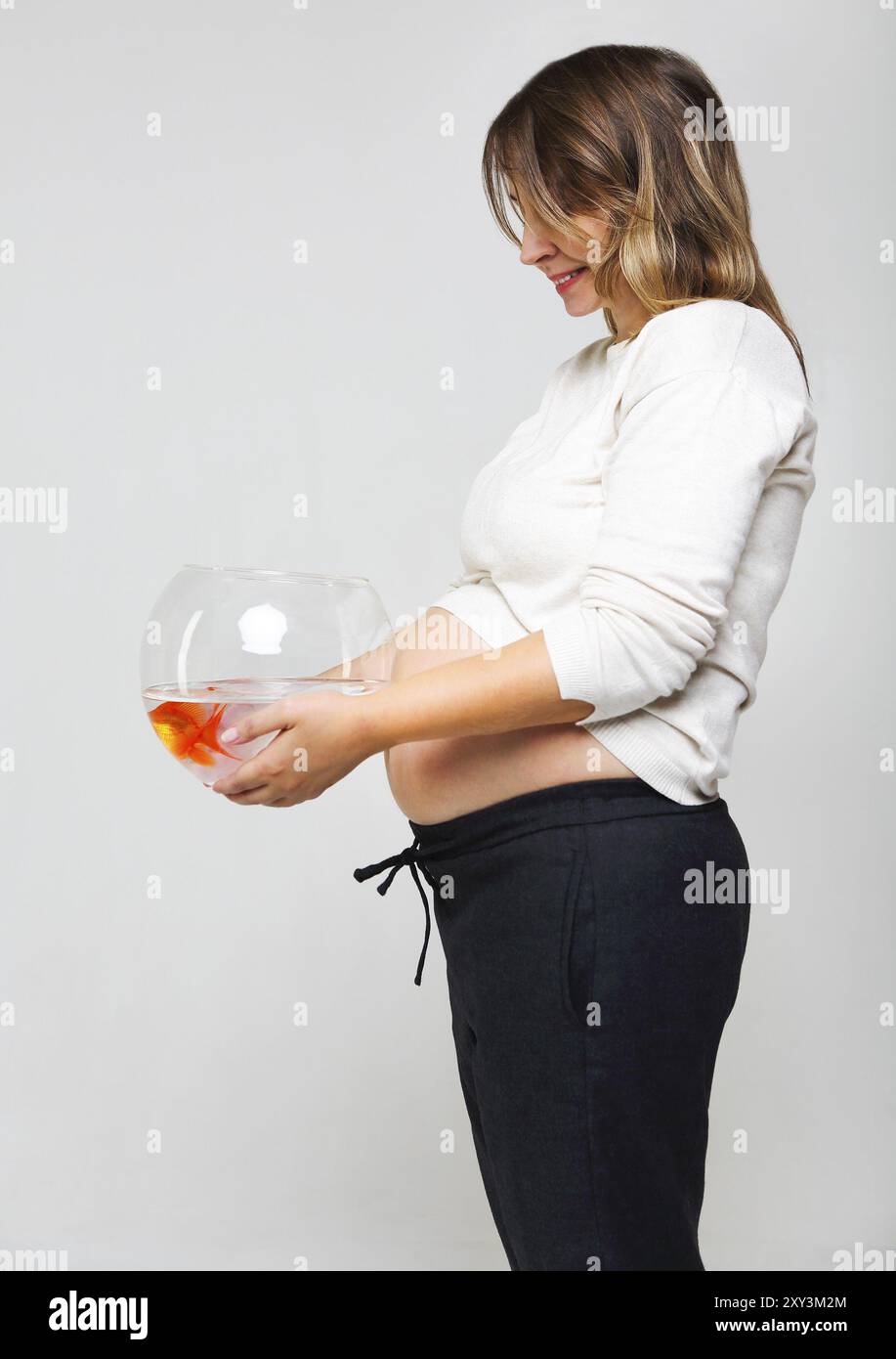 Glücklich schwanger Frau ein Goldfischglas mit einem Goldfisch in ihren Händen hält. Pflege und Liebe Konzept Stockfoto