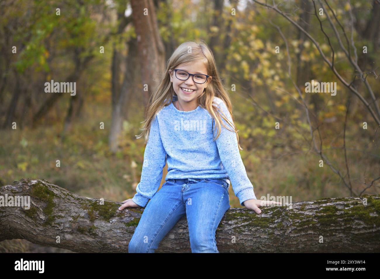 Porträt einer blonde Mädchen mit Brille draußen im Park auf der Herbst park Hintergrund sitzen auf dem Baum Stockfoto