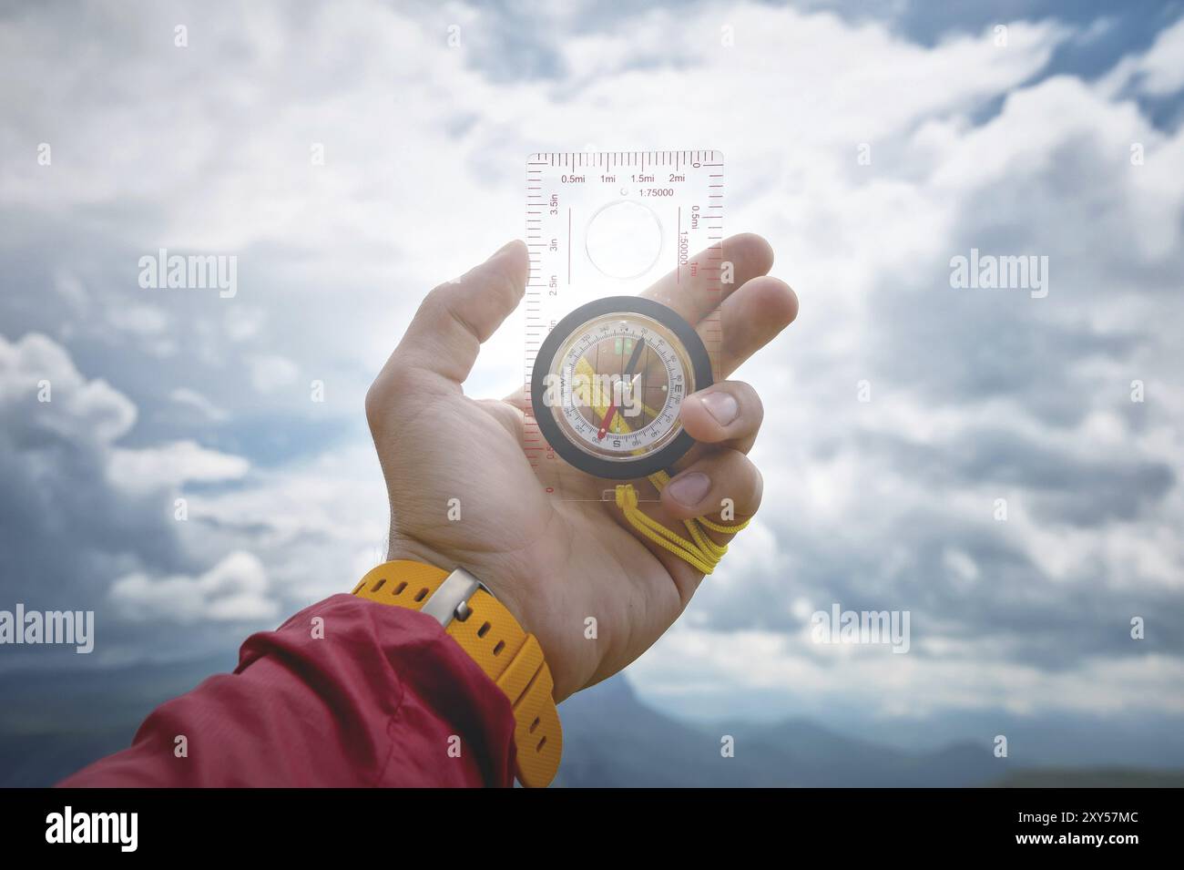 Männliche Hand hält einen magnetischen Kompass auf dem Hintergrund des Himmels mit Wolken. Das Konzept des Reisens und des Findens des Lebenswegs Stockfoto