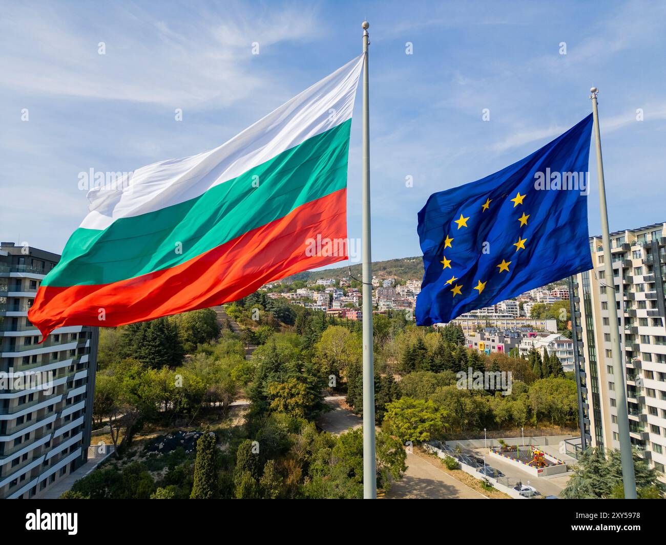 Die Flaggen der Europäischen Union und Bulgariens schweben Seite an Seite über einer Küstenstadt mit Meer und Stadtlandschaft im Hintergrund. Das Bild Stockfoto