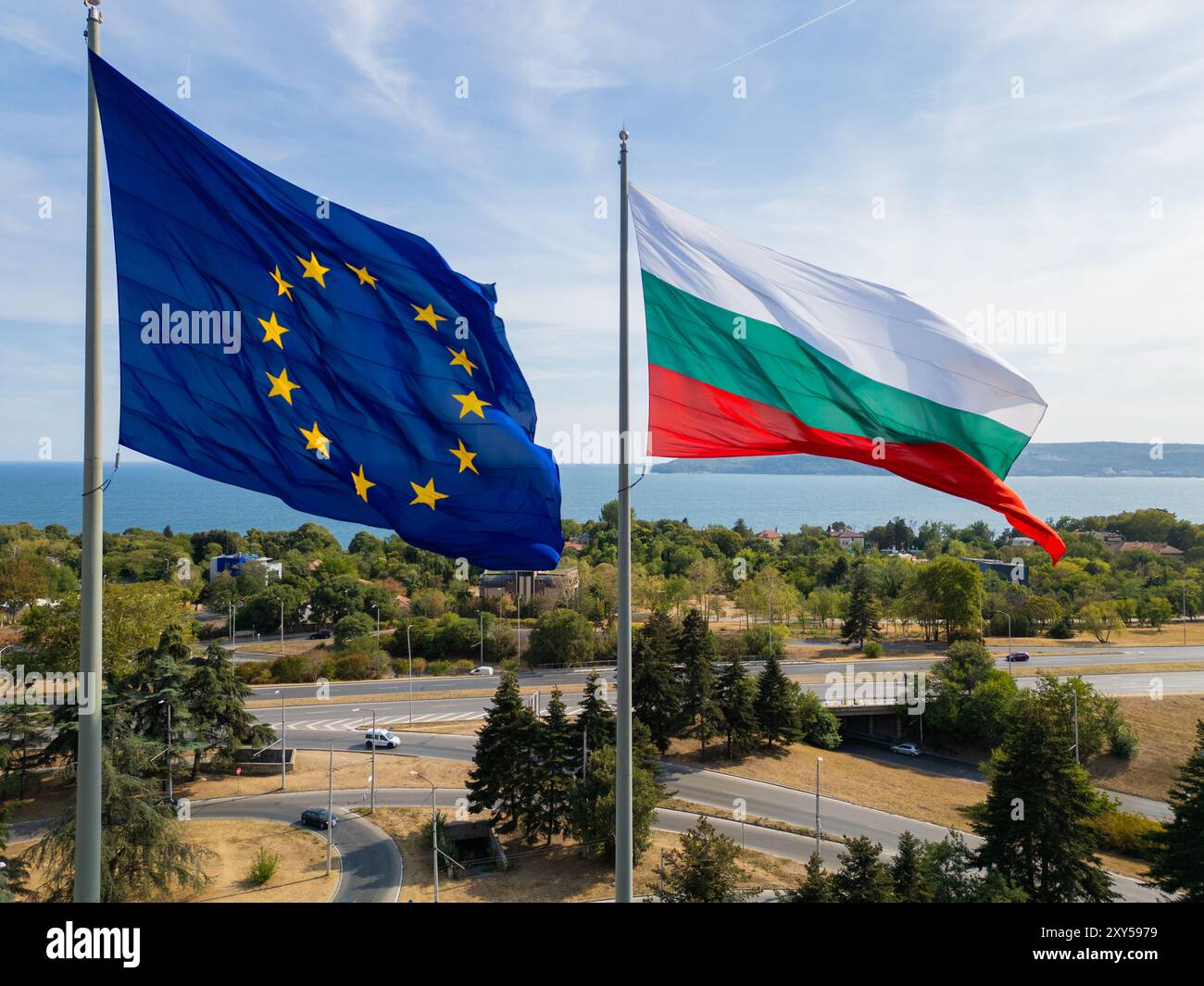 Die Flaggen der Europäischen Union und Bulgariens schweben Seite an Seite über einer Küstenstadt mit Meer und Stadtlandschaft im Hintergrund. Das Bild Stockfoto