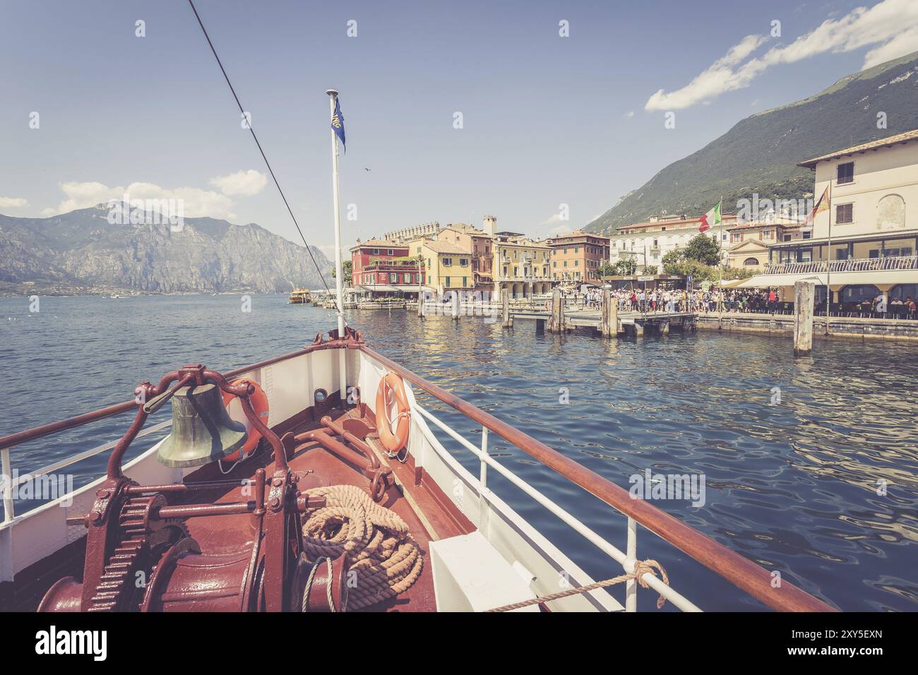 Bug eines Bootes mit Bootsglocke auf einer Bootstour. Blaues Wasser, Bergkette und süßes kleines Dorf am Gardasee, Italien, Europa Stockfoto