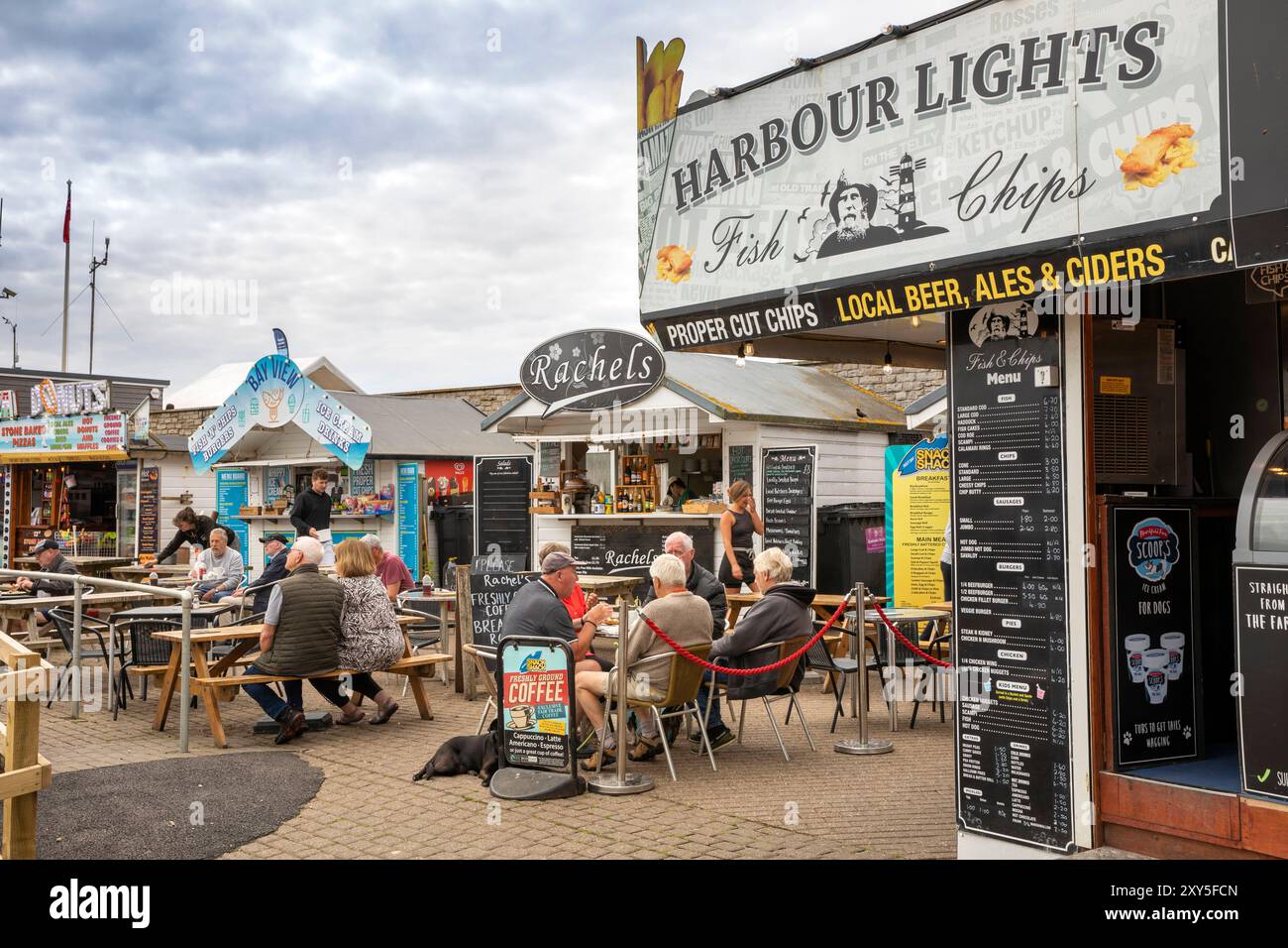 Großbritannien England, Dorset, Bridport, West Bay, Besucher an Tischen in den Cafés von Harbourside Stockfoto