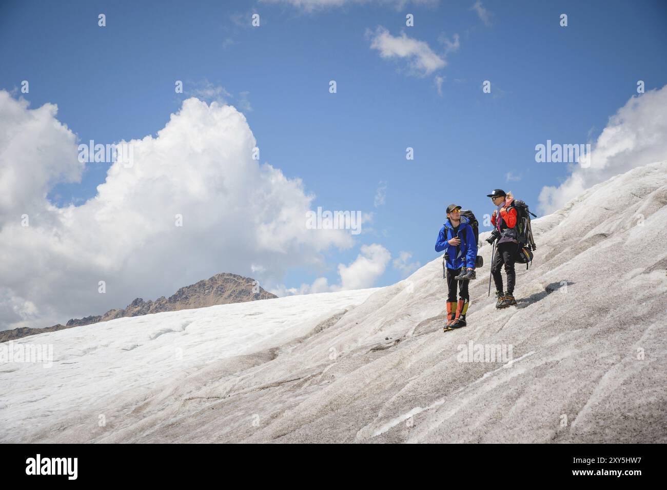 Zwei Touristen, ein Mann und eine Frau mit Rucksäcken und Katzen an den Füßen, stehen auf dem Eis im Hintergrund der Berge des Himmels und der Wolken. Komm Stockfoto