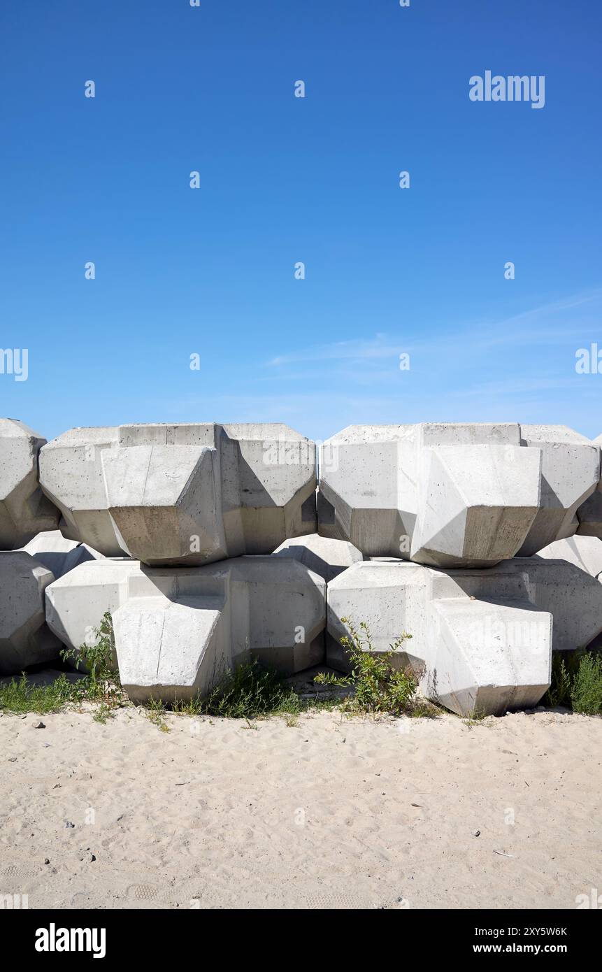 Wellen, die Betonblöcke am Strand ableiten. Stockfoto