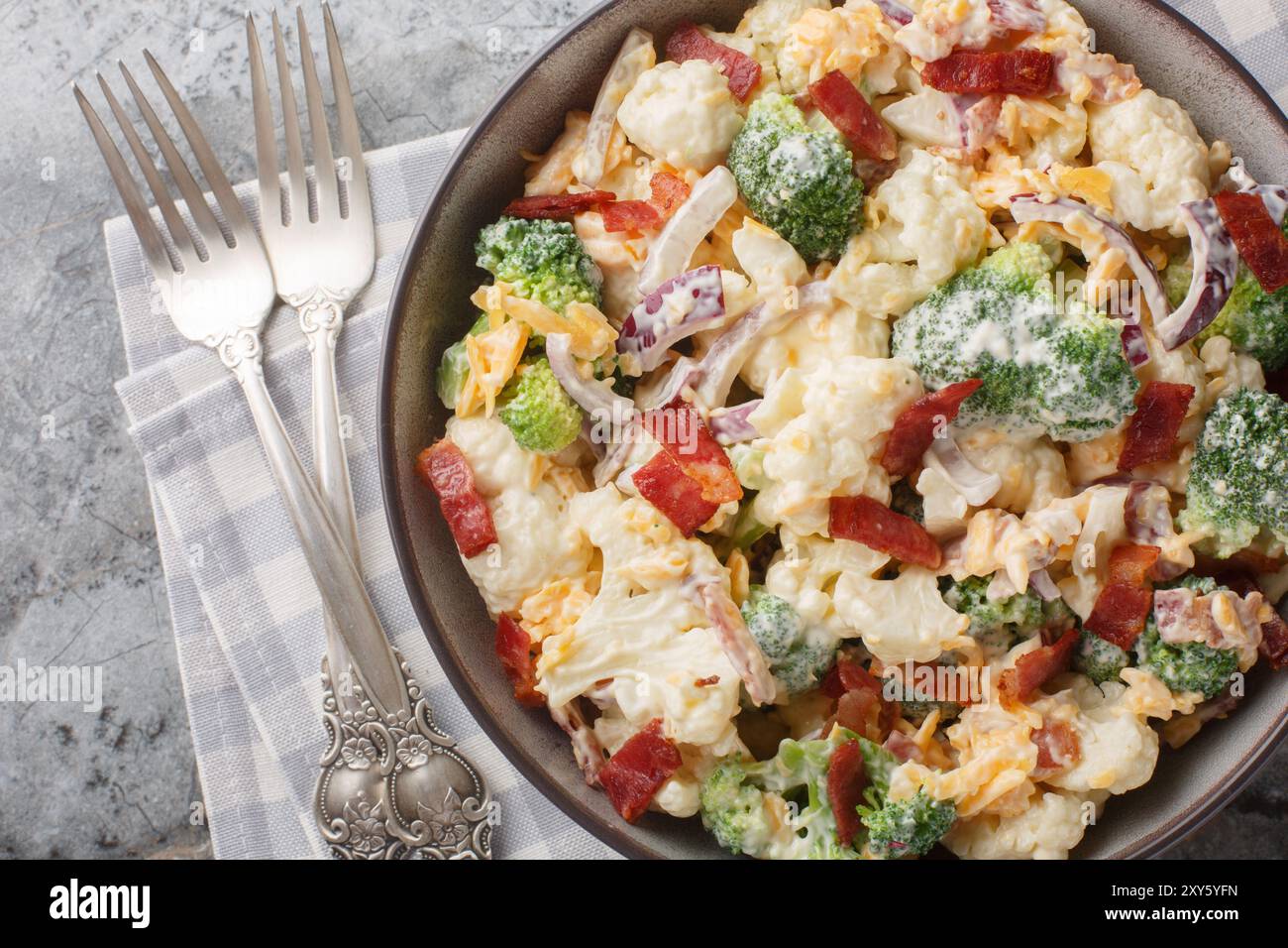 Cremiger Brokkoli-Blumenkohlsalat mit gebratenem Speck, roten Zwiebeln, Käse und Mayonnaise-Dressing in der Schüssel auf dem Tisch. Horizontale Draufsicht fr Stockfoto