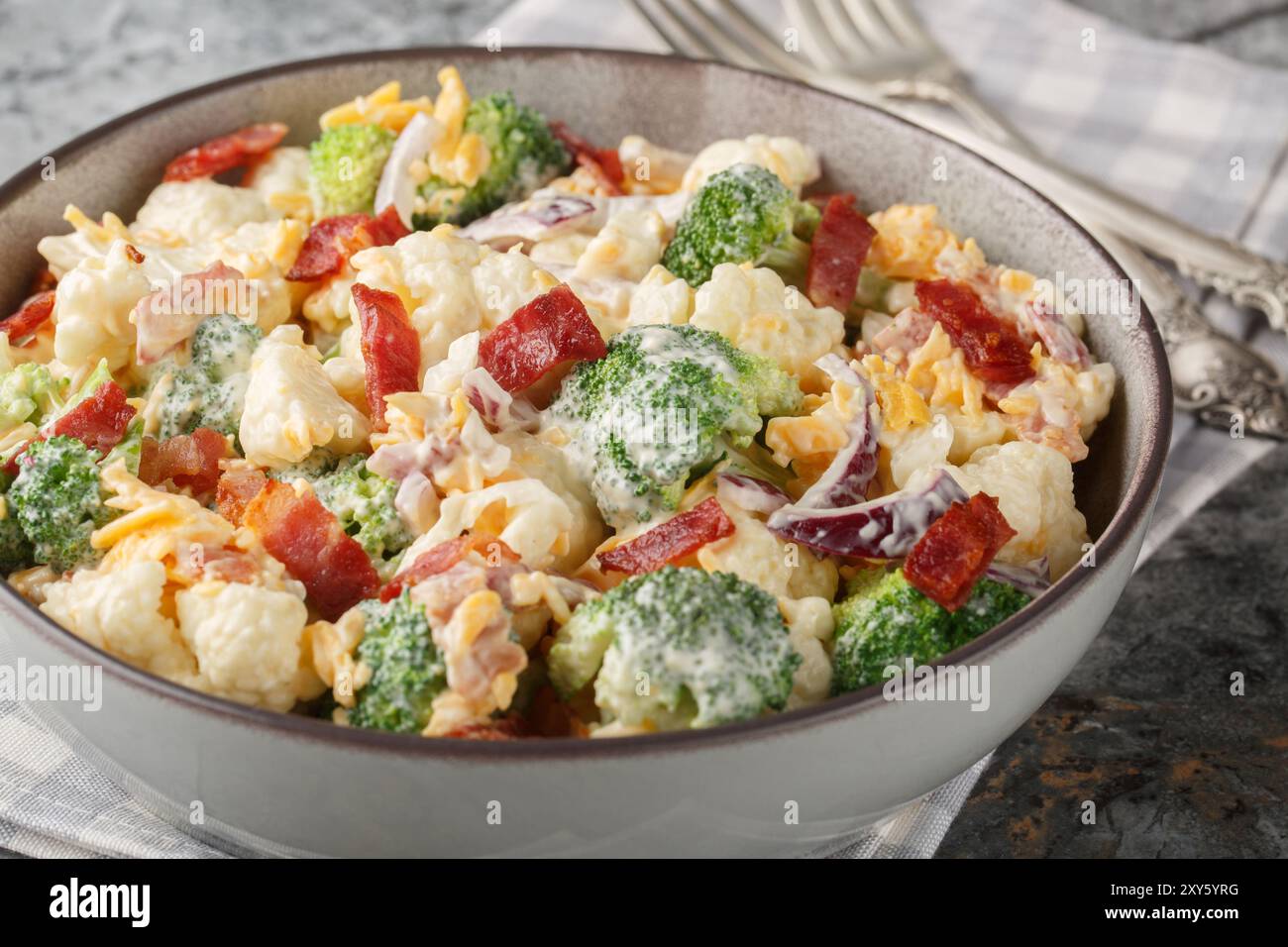 Cremiger Brokkoli-Blumenkohlsalat mit gebratenem Speck, roten Zwiebeln, Käse und Mayonnaise-Dressing in der Schüssel auf dem Tisch. Horizontal Stockfoto