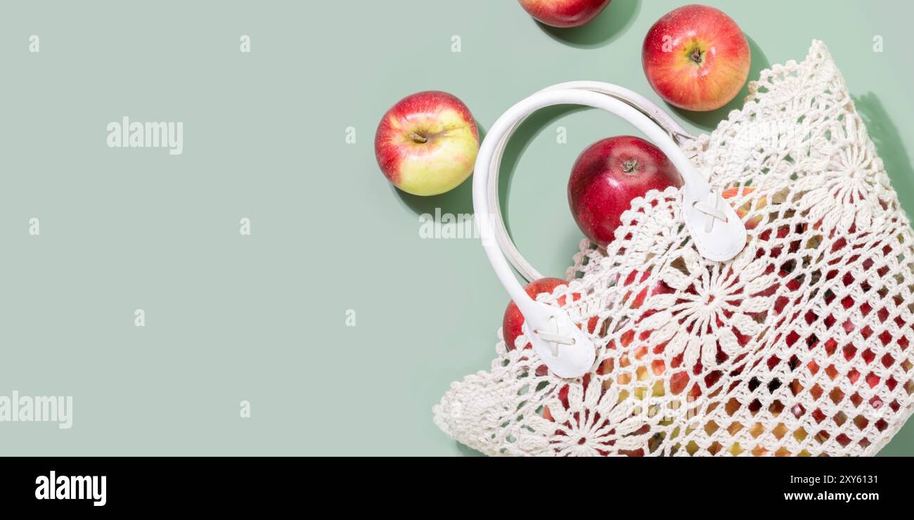 Rote Äpfel, die aus der gehäkelten Tasche auf pastellgrünem Hintergrund verschüttet werden Stockfoto