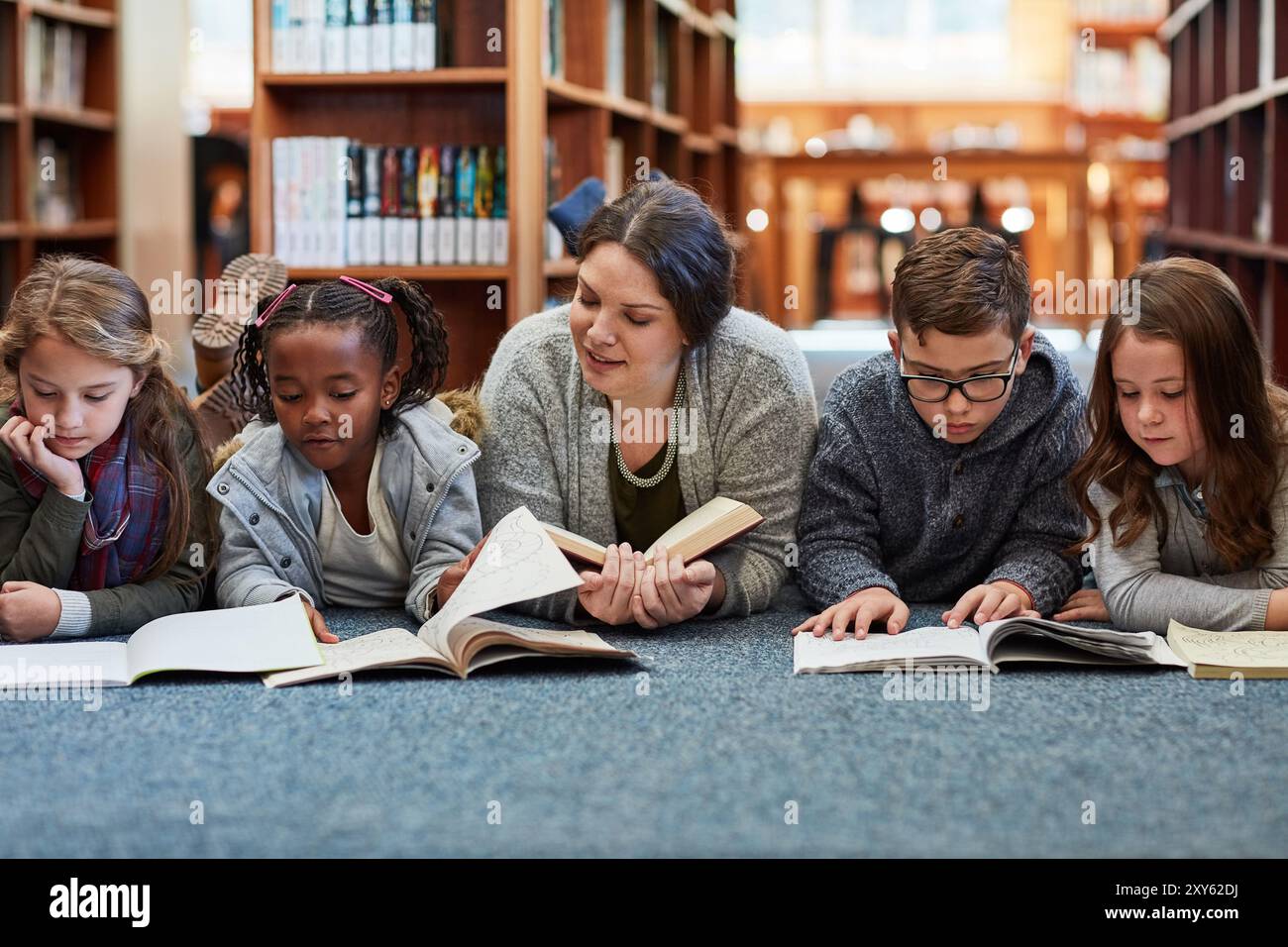 Frau, Lehrerin und Lesebuch für Kinder auf dem Boden, Bildung und Fantasy-Literatur-Fiktion. Weibliche Person, Freiwillige in der Bibliothek und Geschichten erzählen Stockfoto