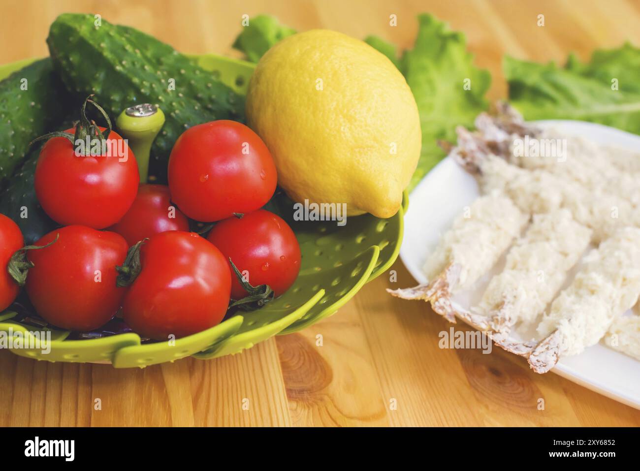 Rohe Garnelen in Teig, bereit zum Rösten, neben einem Korb Gurken, Zitronengurken und Tomaten vor dem Hintergrund von Salatblättern auf einem Holz Stockfoto