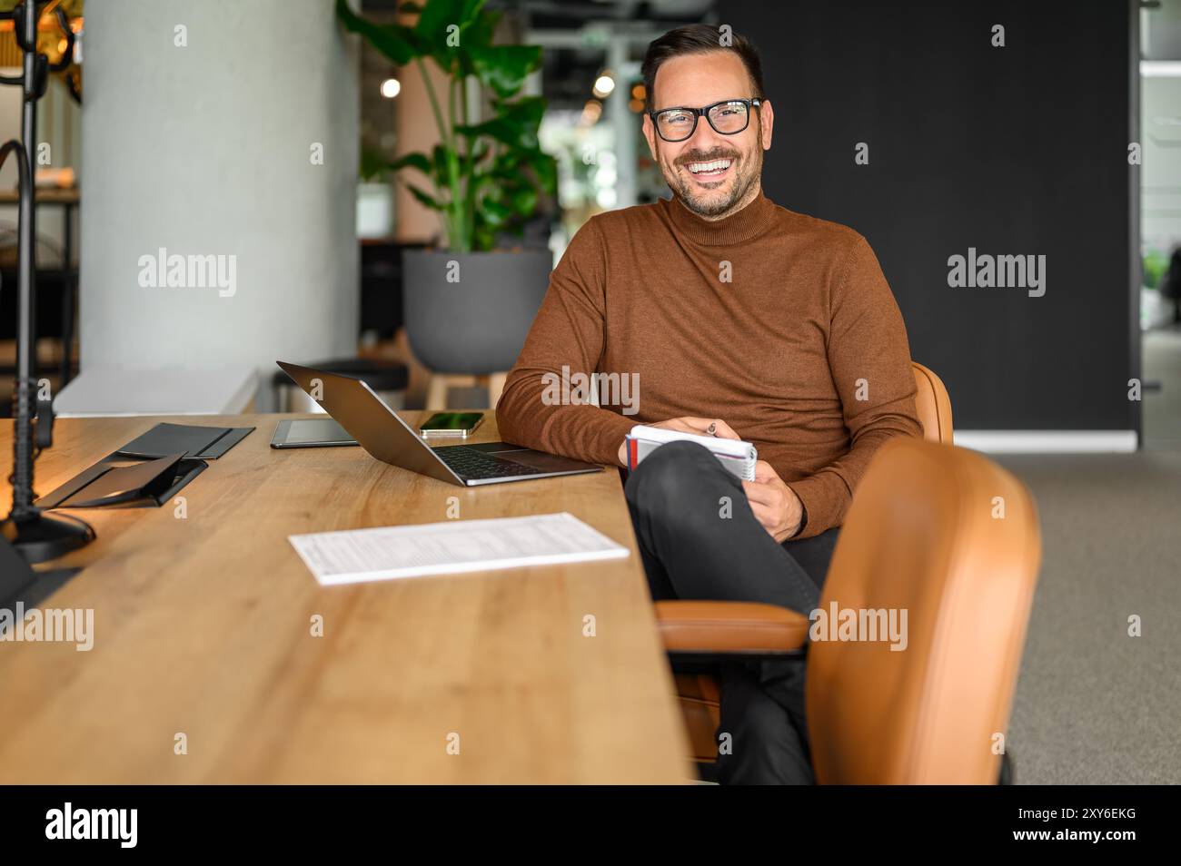 Porträt eines inspirierten männlichen Unternehmers in Brille, der über einem Laptop arbeitet, während er im Büro am Schreibtisch sitzt Stockfoto