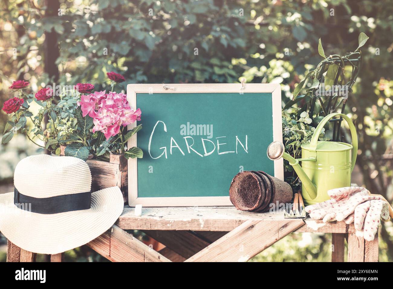 Kleine Tafel mit Beschriftungen Garten auf Holztisch unter grünen Pflanzen in Tontöpfen Strohhut und Metall-Gießkanne Stockfoto