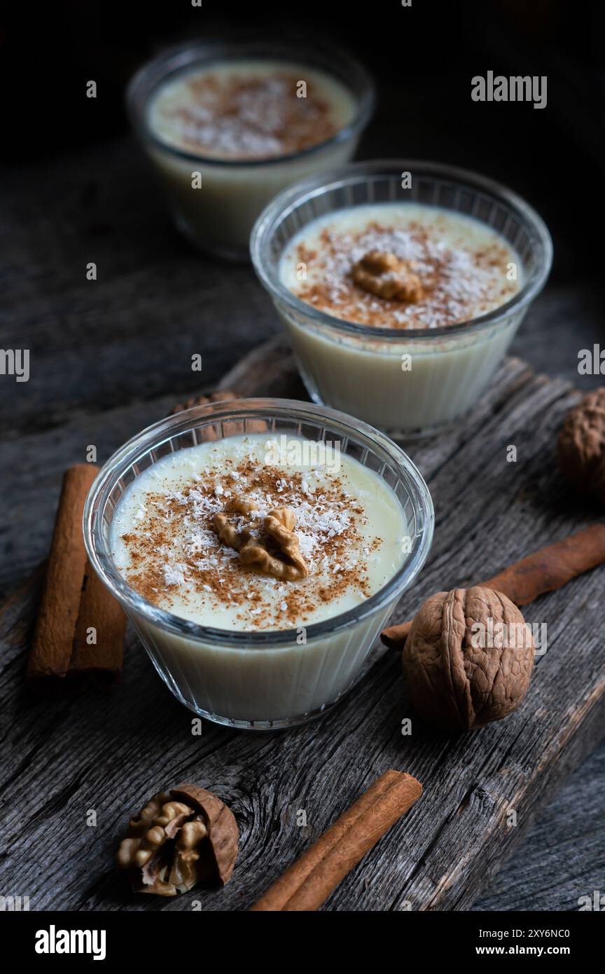 Pudding in Glasschale mit Zimt und Walnuss auf rustikalem Tisch, Milchdessert Stockfoto