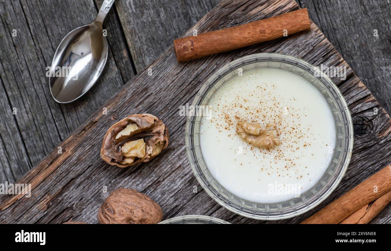 Pudding in Glasschale mit Zimt und Walnuss auf rustikalem Tisch, Milchdessert Stockfoto