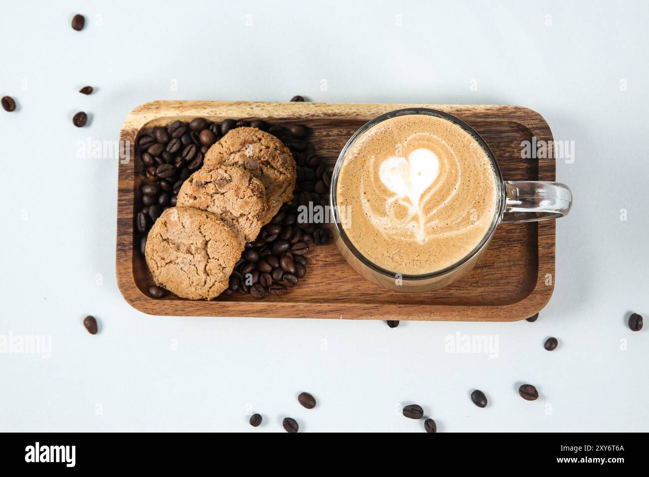 Tasse Kaffee mit Herzform im Schaum mit Kaffeebohnen und Keks auf weißem Hintergrund Stockfoto