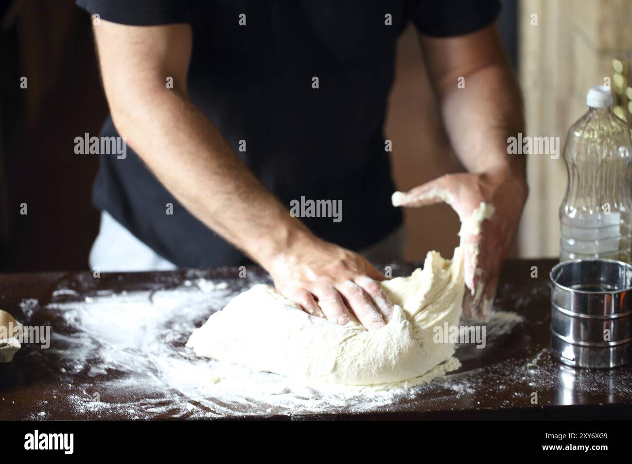 Männliche Hände kneten frischen Teig auf dem Küchentisch. Nahaufnahme Stockfoto