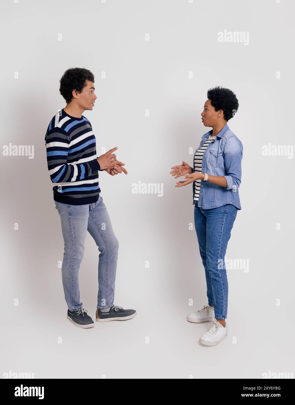 Seitenansicht eines jungen Paares, das sich ansieht und darüber spricht, während er über weißem Hintergrund steht Stockfoto