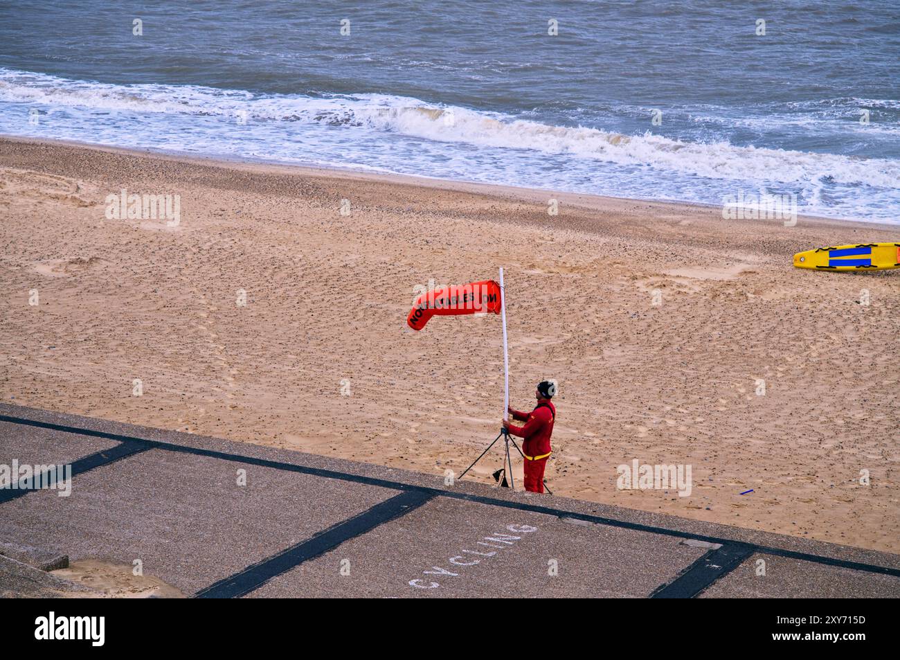 Ein RNLI-Rettungsschwimmer zieht an einem windigen Tag eine Windsocke ohne aufblasbare Windsocke am Southwold Beach Stockfoto