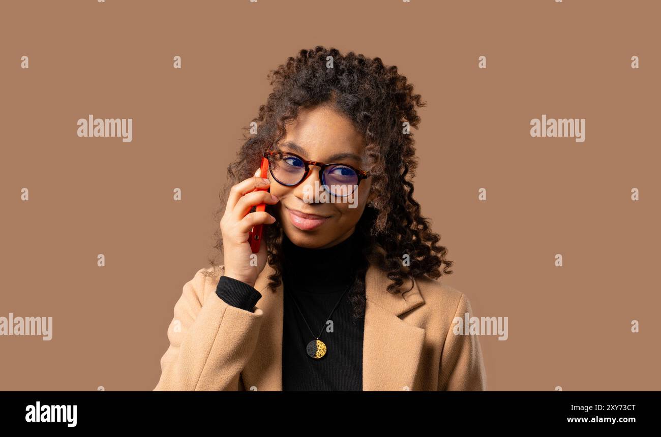 Attraktive multirassische Frau, die telefoniert, netter Witz, lächelnd. Junge Geschäftsfrau auf beigefarbenem Hintergrund. Telefonieren mit dem Smartphone. Hohe Qualität Stockfoto