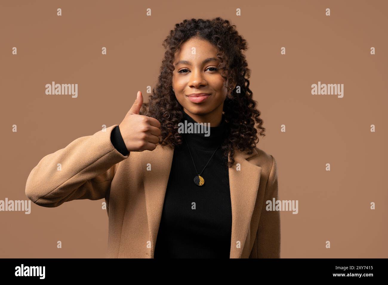 Stilvolle Frau mit Handzeichen, Daumen hoch Geste. Glückliche Dame, richtige perfekte Wahl, sehr viel, beigefarbener Hintergrund. Positives weibliches Modell lächelt Stockfoto