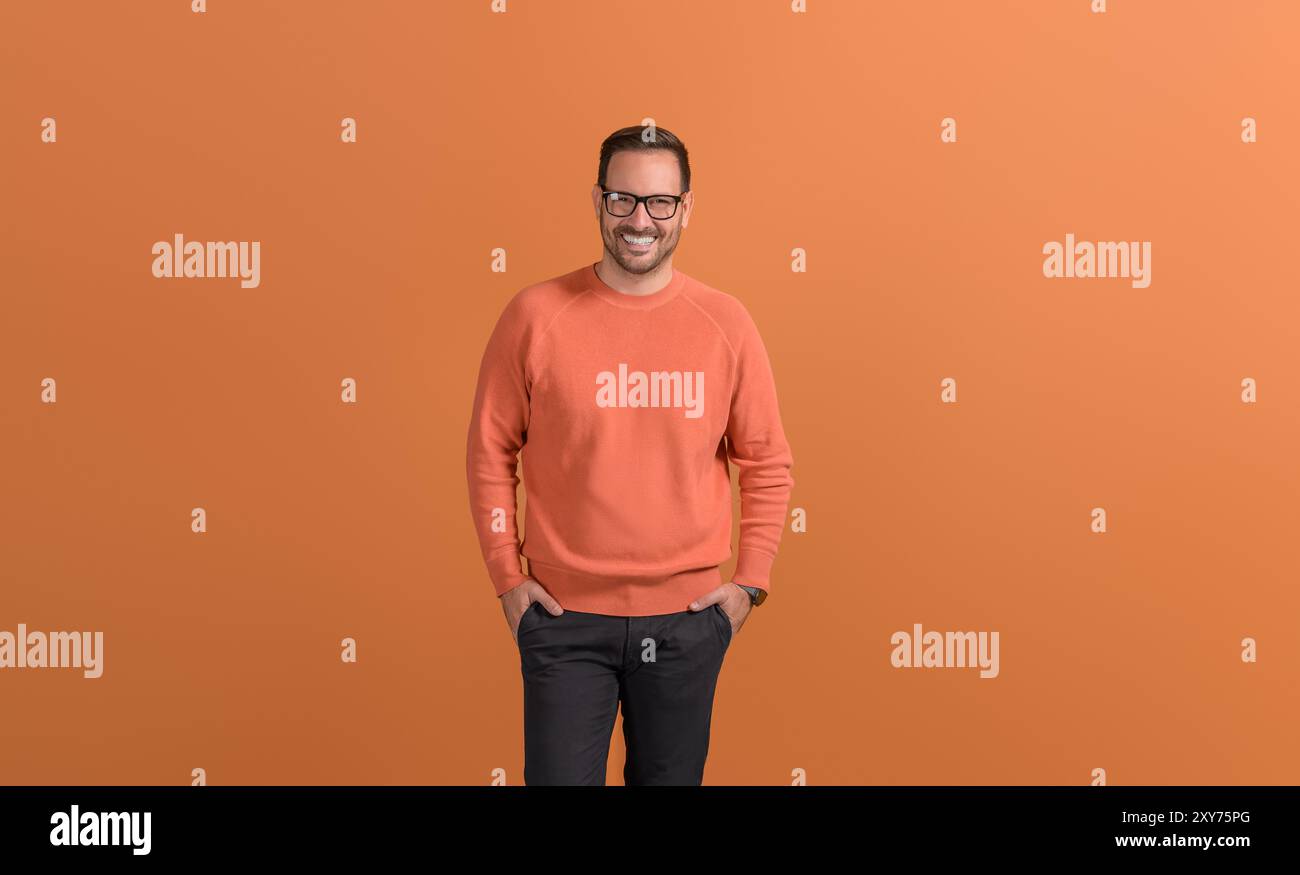 Porträt eines lächelnden männlichen Freelancers mit Händen in Taschen, die selbstbewusst auf orangefarbenem Hintergrund stehen Stockfoto