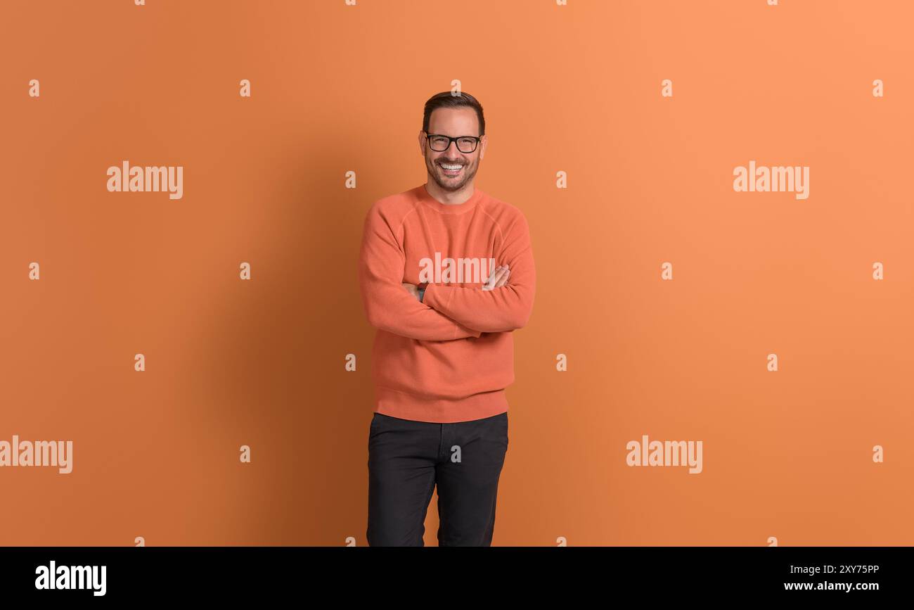 Porträt eines entschlossenen jungen Geschäftsmannes mit überkreuzten Armen, der selbstbewusst auf orangefarbenem Hintergrund posiert Stockfoto