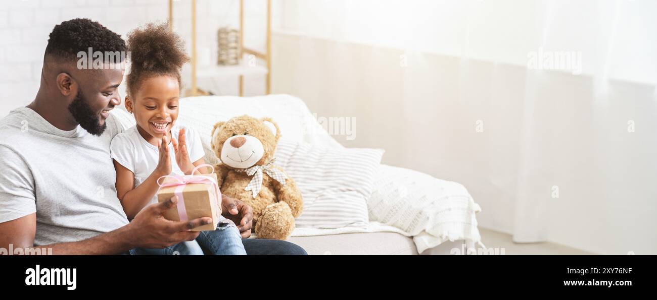 Vater und Tochter packen freudig ein Geschenk zusammen aus Stockfoto