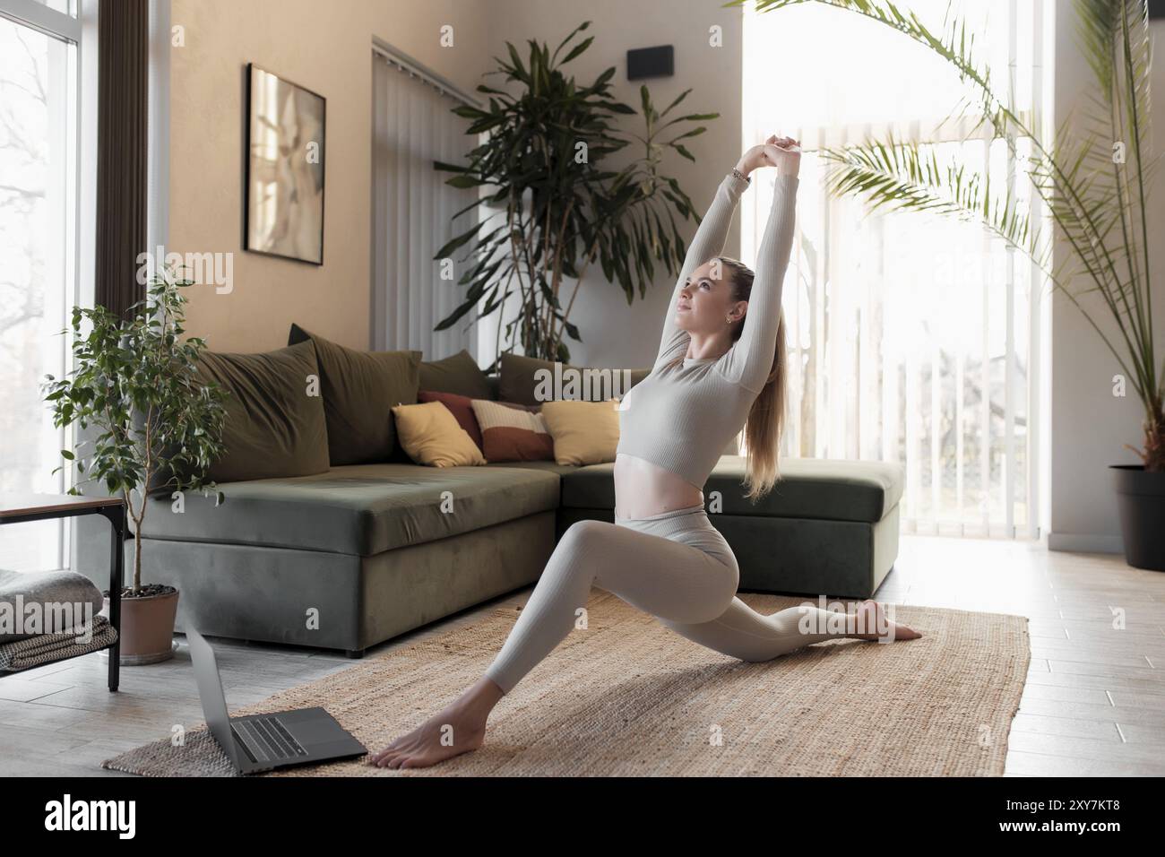 Hübsche kaukasische junge Frau, die zu Hause im Wohnzimmer ein Workout macht und Yoga praktiziert, während sie sich einen Videokurs für Yoga am Laptop im Praktikanten ansieht Stockfoto