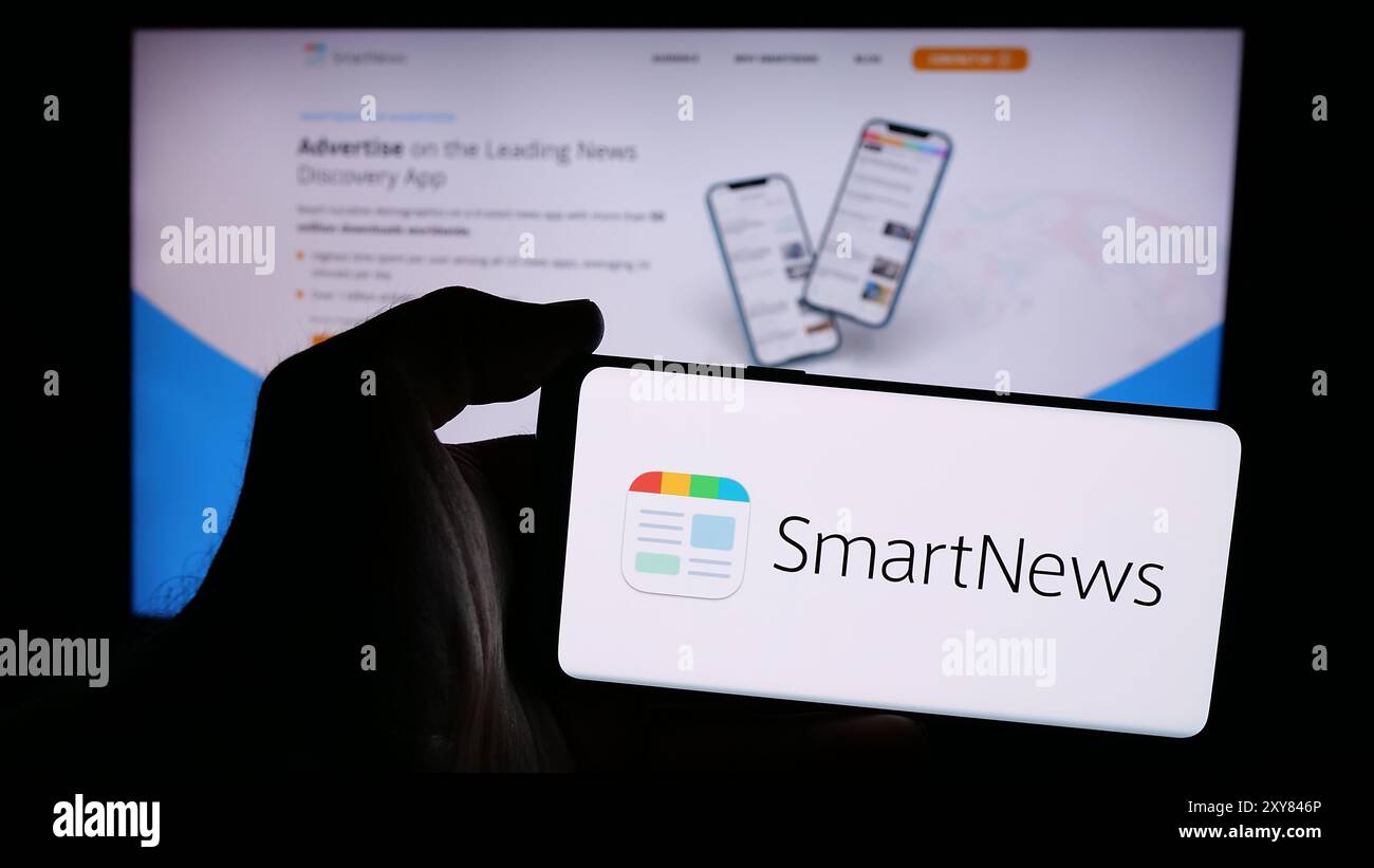 Person mit Smartphone und Logo der japanischen Nachrichtenagentur SmartNews Inc. Vor der Website. Schwerpunkt auf dem Display des Telefons. Stockfoto