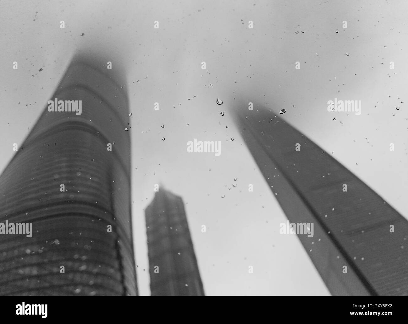 Der flache Blick auf den Shanghai Tower und die benachbarten Wolkenkratzer verschwimmen an einem regnerischen Tag in Wolken, wenn man durch ein Autofenster mit Regentropfen sieht Stockfoto