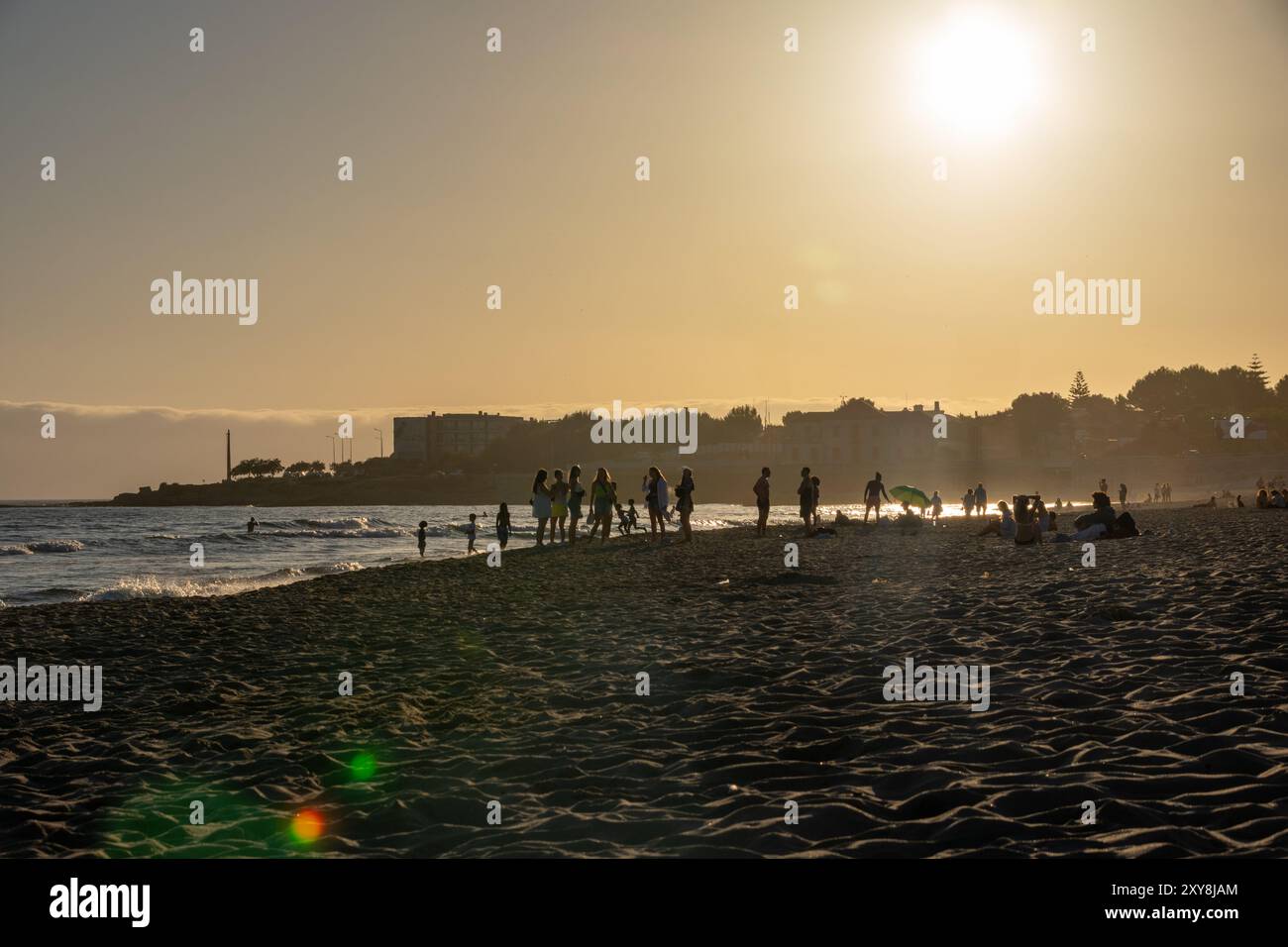 Ein goldener Sonnenuntergang am Strand von Carcavelos, Portugal, wo Silhouetten von Menschen, die die Wellen und den Sand genießen, auf das warme Leuchten der untergehenden Sonne treffen. Stockfoto