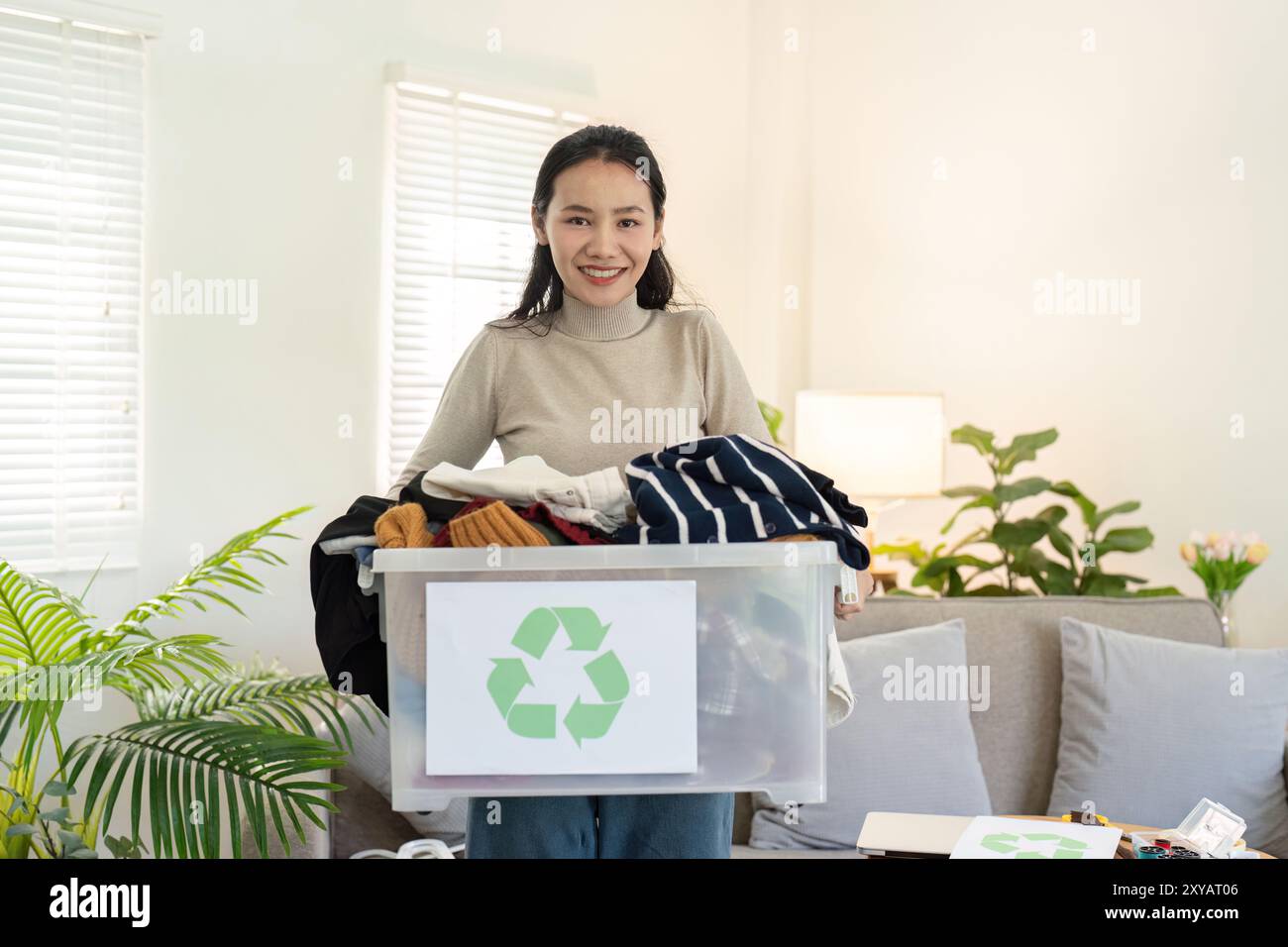 Lächelnde Frau mit recyceltem Kleiderbehälter. Umweltfreundliche Mode und Wiederverwendung Stockfoto