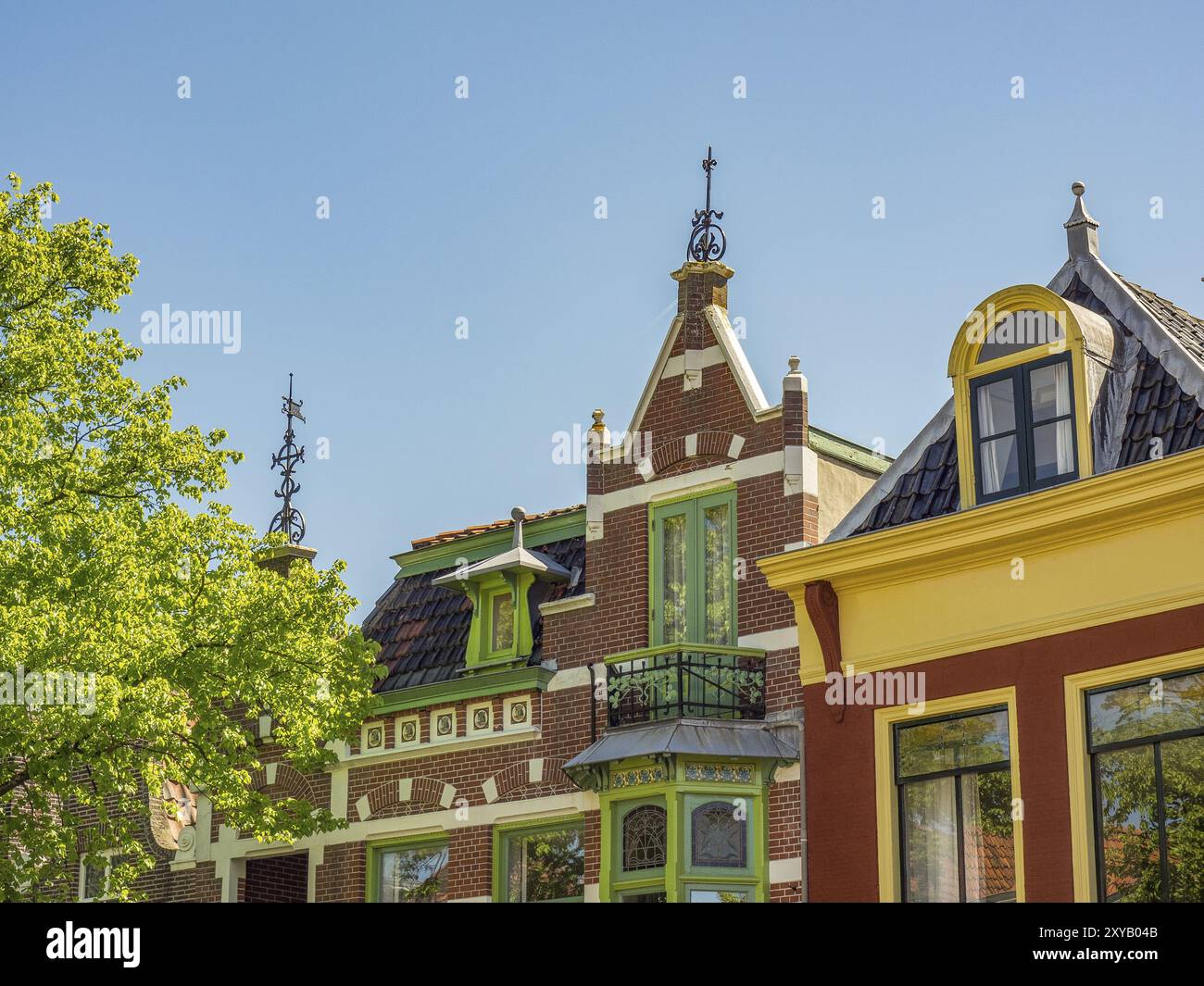 Bäume und farbenfrohe historische Gebäude mit grünen Fensterläden und Dekorationen unter klarem Himmel, alkmaar, niederlande Stockfoto