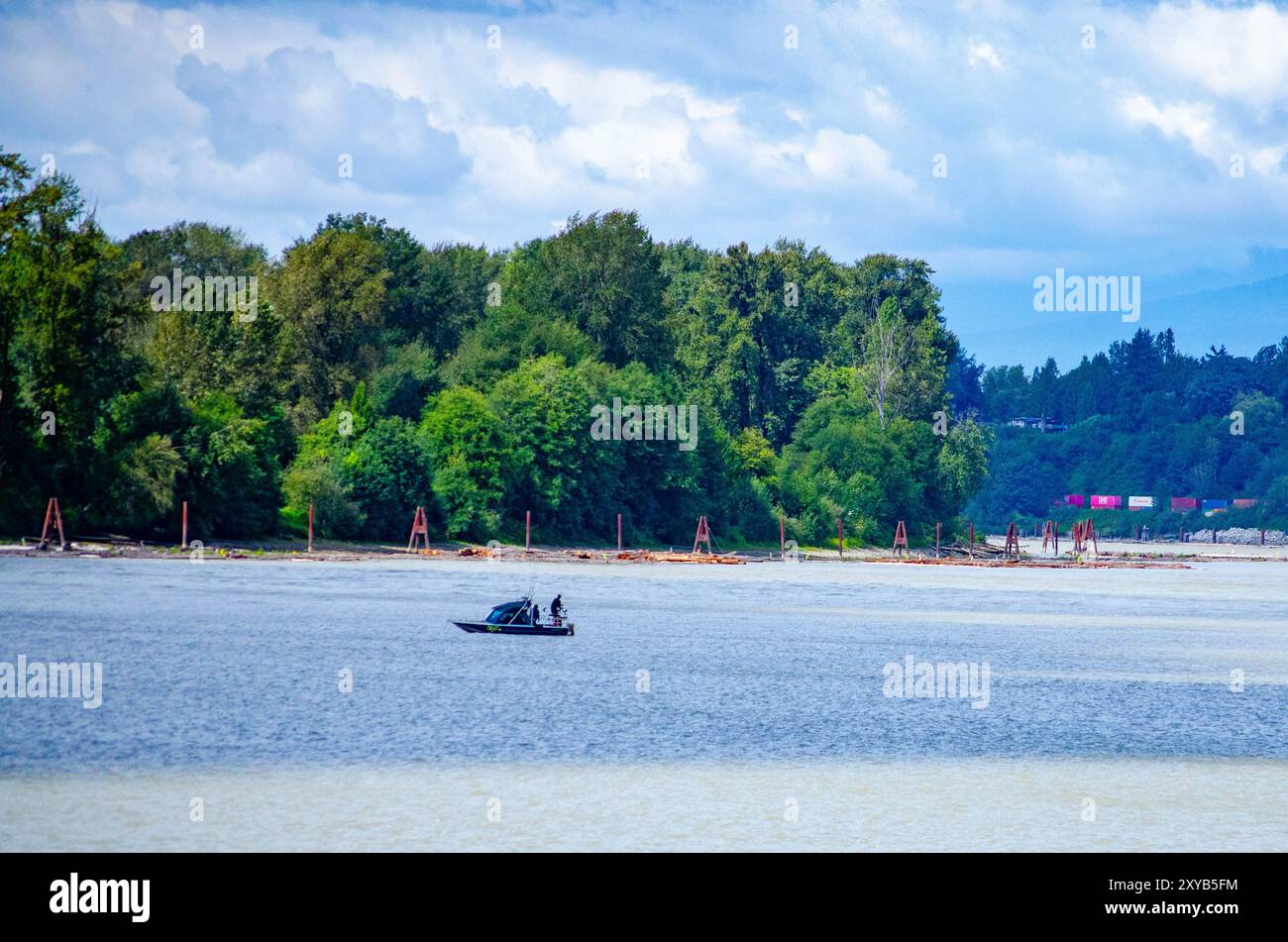 Kleines Fischerboot auf dem Fluss mit bewaldeter Küste Stockfoto