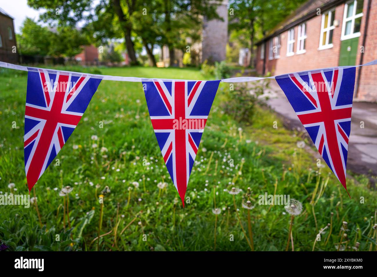 Englische Union Jack Flaggen, patriotische britische Fahnenbanner hängen, winken mit einem alten Kirchenhof, Schulhof im Hintergrund, sonniger Tag, keine Leute. Stockfoto