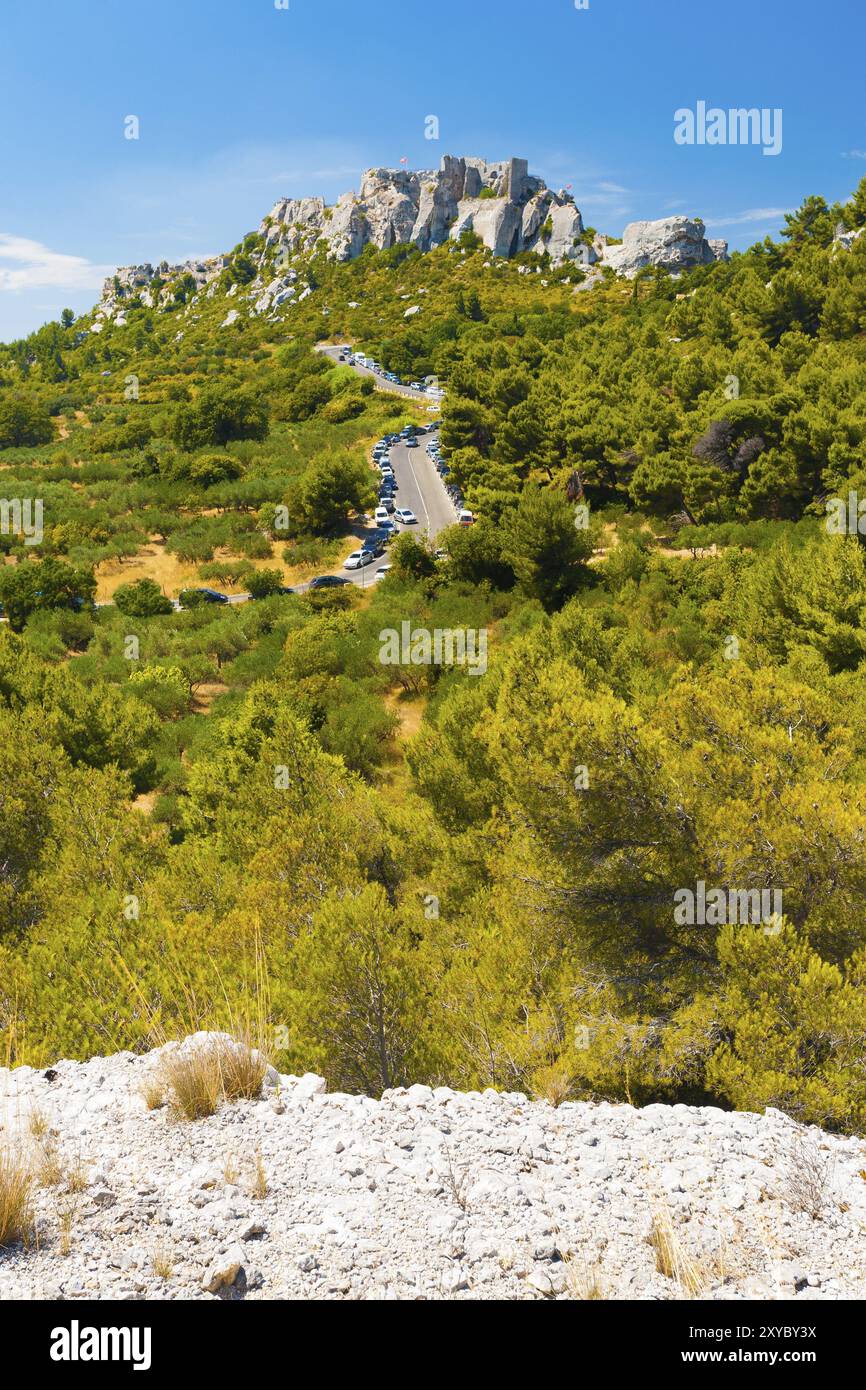 Von einer Klippe aus gesehen führt eine moderne Straße zu den Ruinen des Baux auf einem felsigen Berg in Les Baux de Provence, Frankreich, Europa Stockfoto