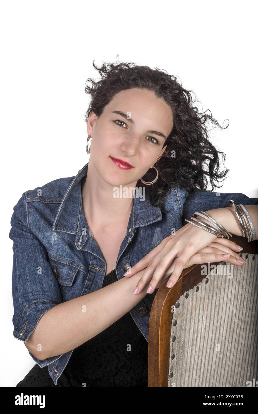 Ein junges Model, Mitte 20, sitzt auf einem hölzernen Stuhl mit einer blauen Jeansjacke Stockfoto