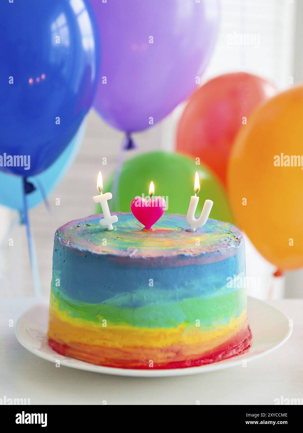 Regenbogen Kuchen und Muffins mit Kerzen geschmückt. Luftballons auf dem Hintergrund Stockfoto