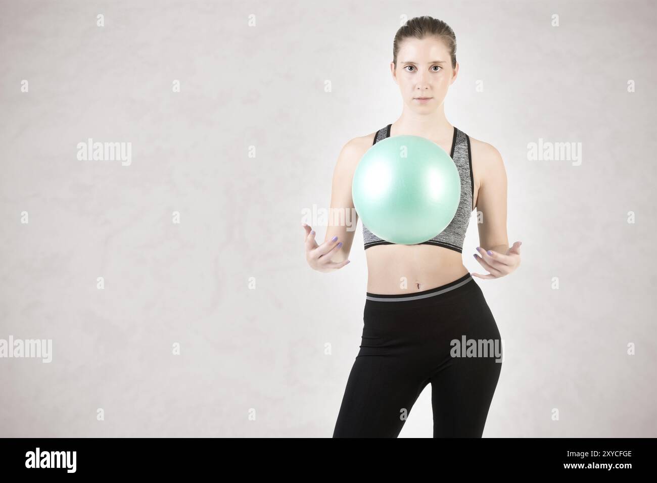 Fit Frau stehen und halten einen Pilates Ball, isoliert in grau Stockfoto