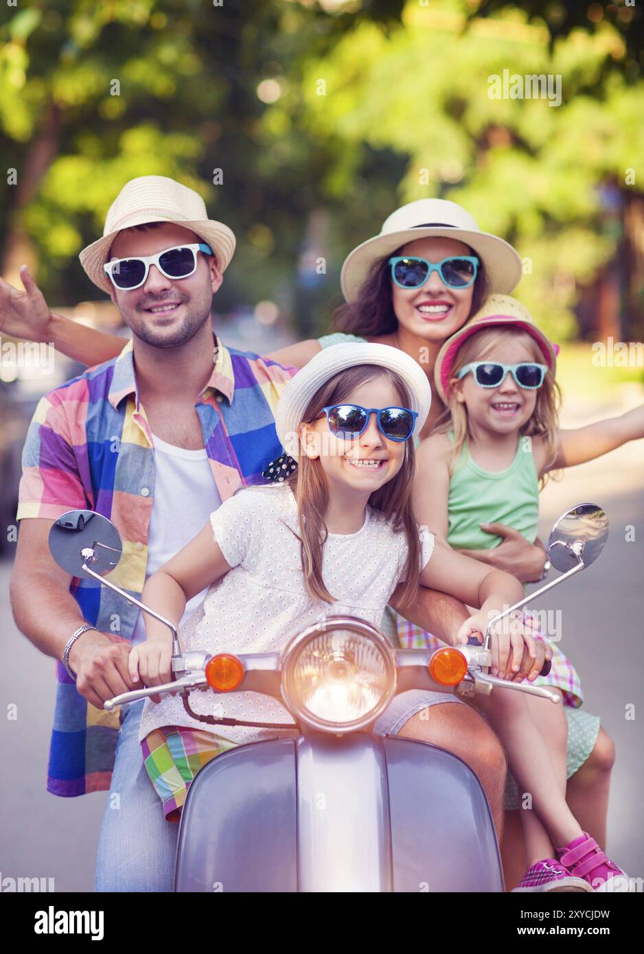 Glückliche junge Familie Motorroller Oldtimer auf der Straße tragen Hüte und Sonnenbrillen. Urlaub und Reisen-Konzept Stockfoto