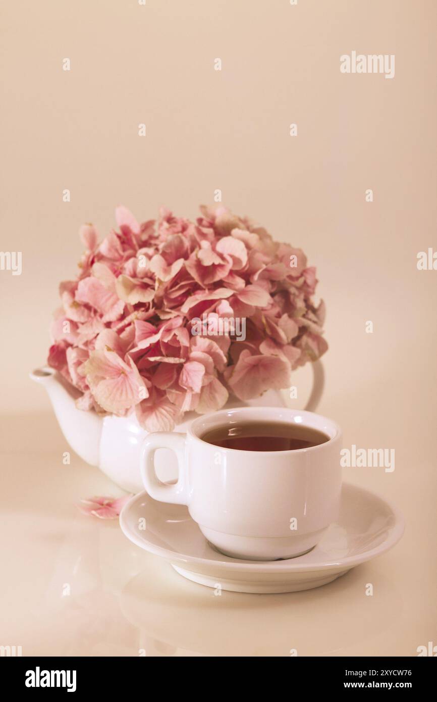 Porzellan-Teekanne und -Tasse für den Tee mit Blütenblättern aus rosa Blumen auf beigem Hintergrund Stockfoto