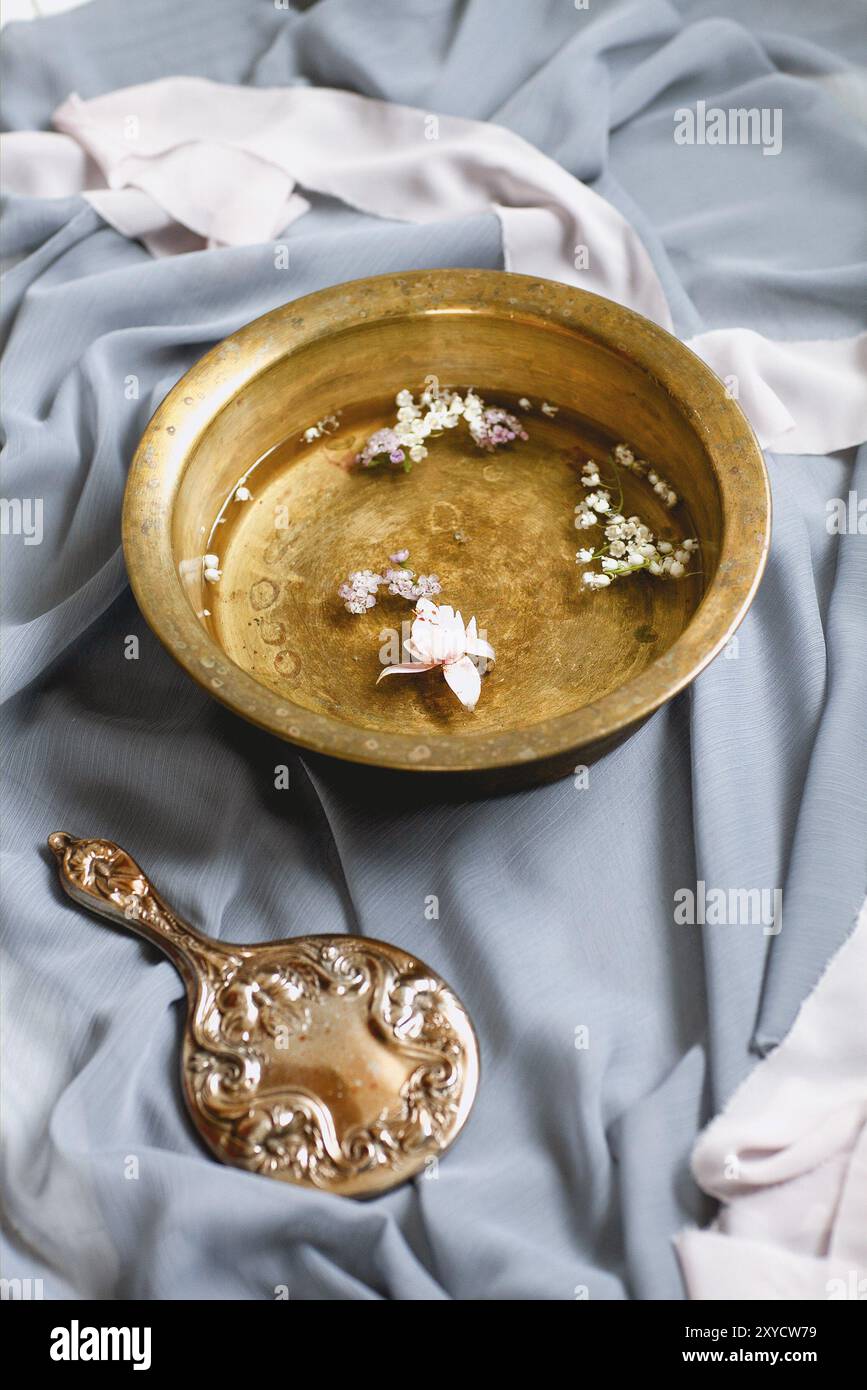 Hoher Winkel der braunen Schüssel mit frischen kleinen Blumenköpfen und Vintage-Handspiegel zwischen filigranen transparenten Pastellfarben und Komposito Stockfoto