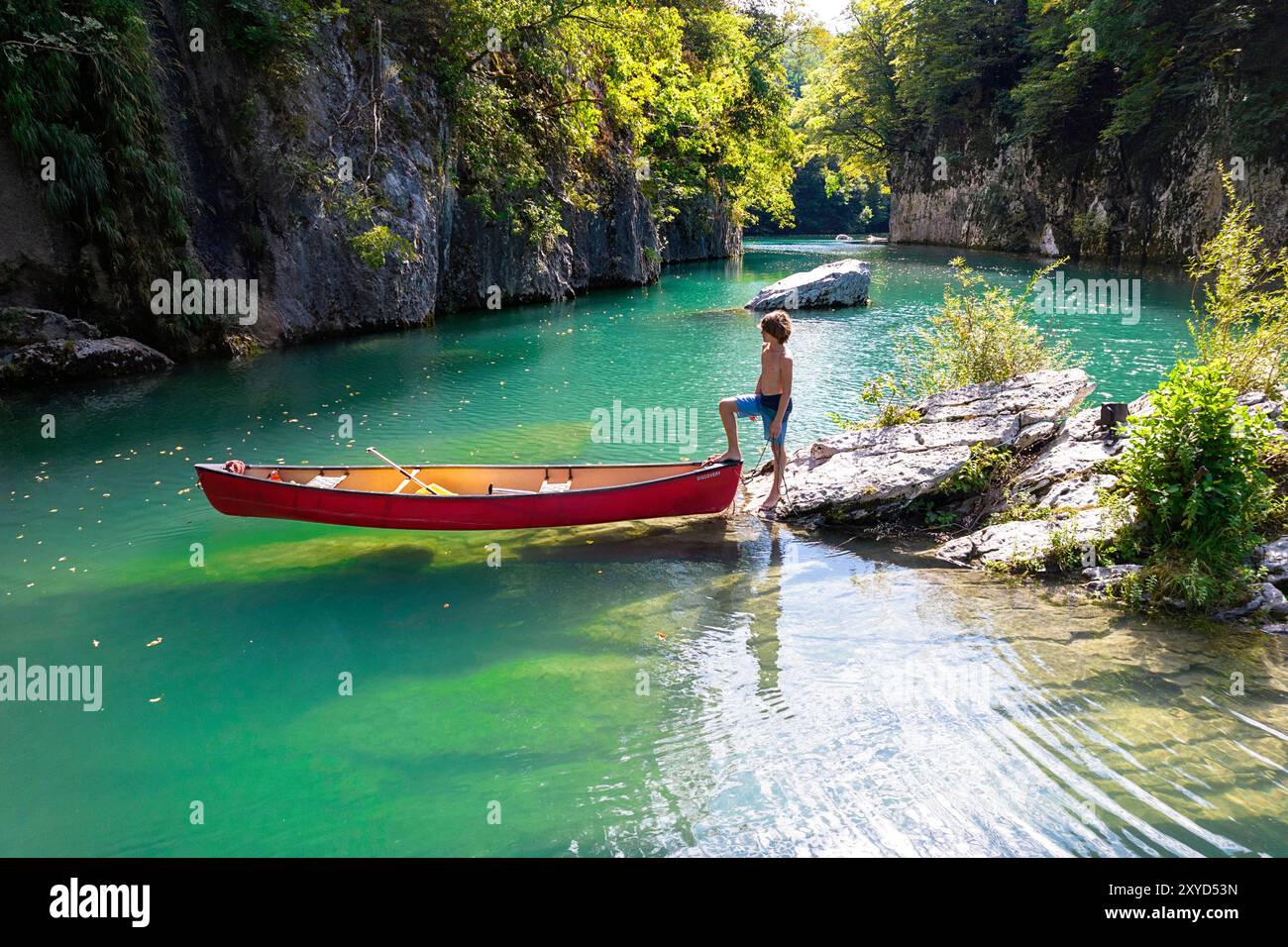 Junge mit seinem Kanu, der auf einem Felsen mitten im Idrijca-Fluss an einem heißen sonnigen Sommertag in der Nähe von Most na Soči, Slowenien, steht. Stockfoto