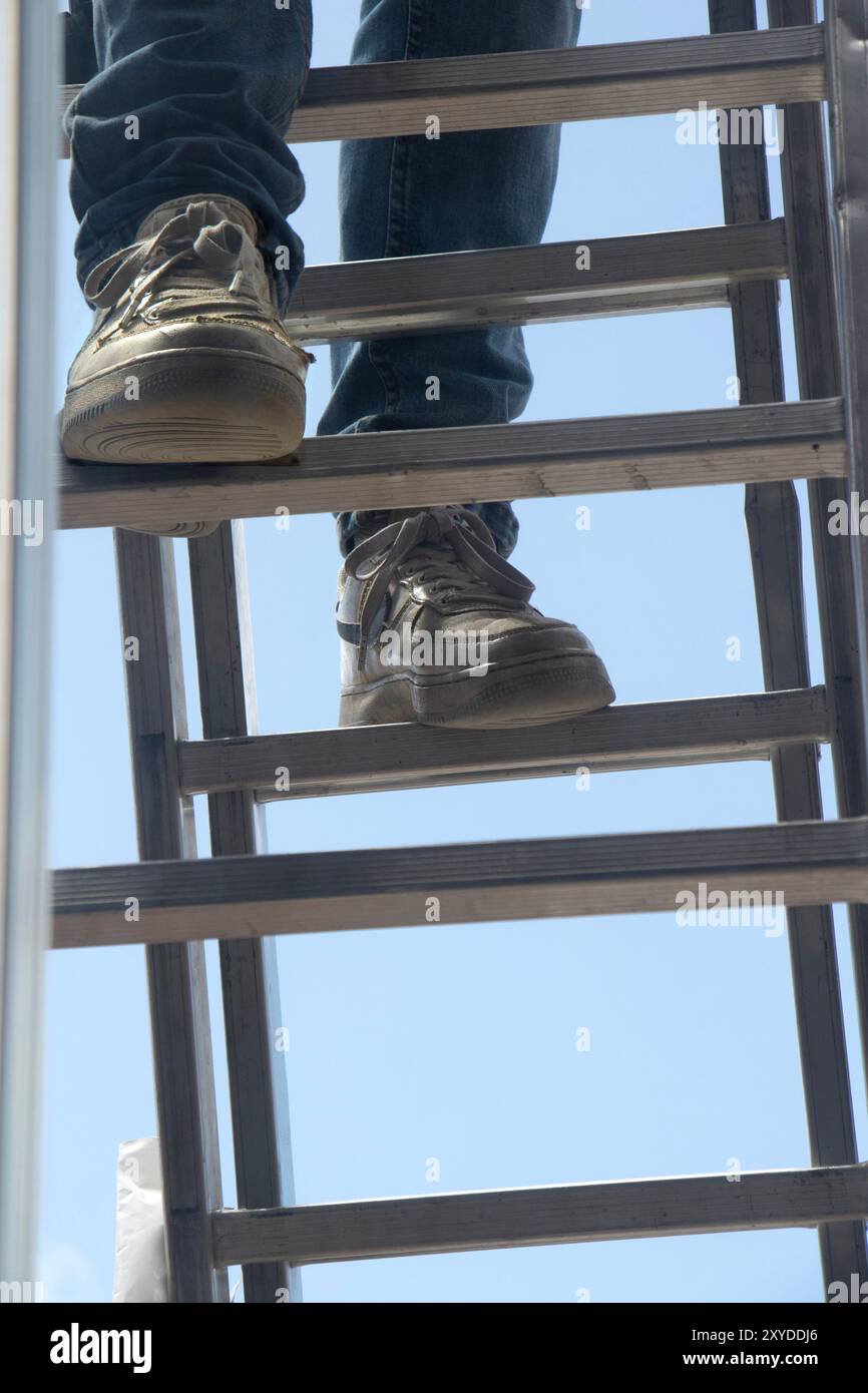 Nahaufnahme einer Person mit Turnschuhen, die eine Metallleiter vor einem klaren blauen Himmel klettert. Gesundheits- und Sicherheitskonzept albufeira portugal Stockfoto