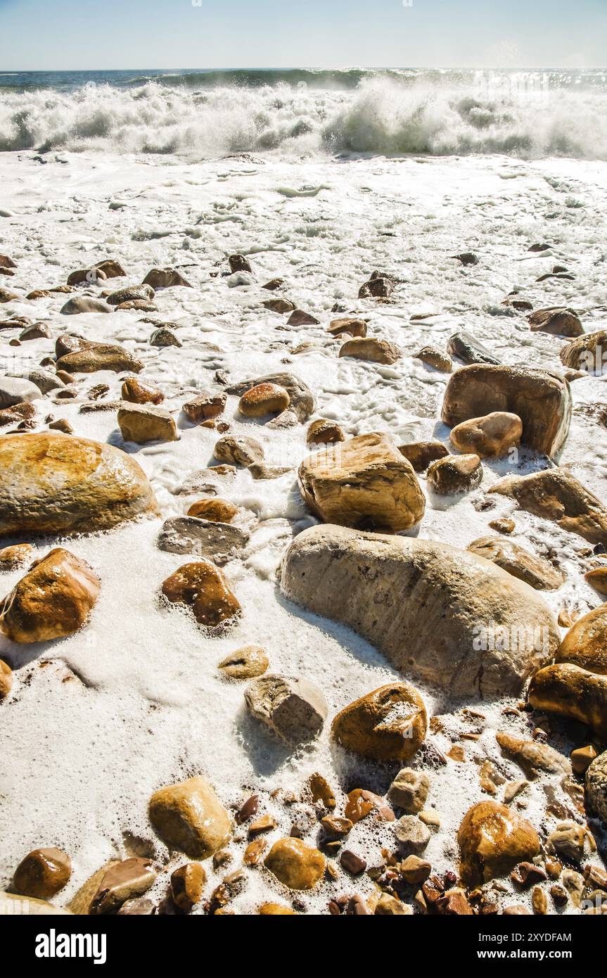 Wellen stürzen an einem felsigen Strand, wenn die Flut hereinbricht, und lassen weiße Wake hinter sich, während das Wasser liegt Stockfoto