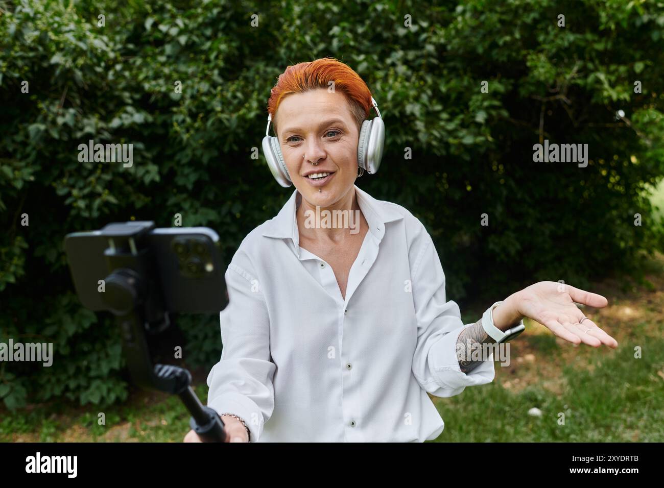 Eine Frau in einem weißen Hemd nimmt ein Video mit einem Smartphone auf, während sie Kopfhörer trägt. Stockfoto