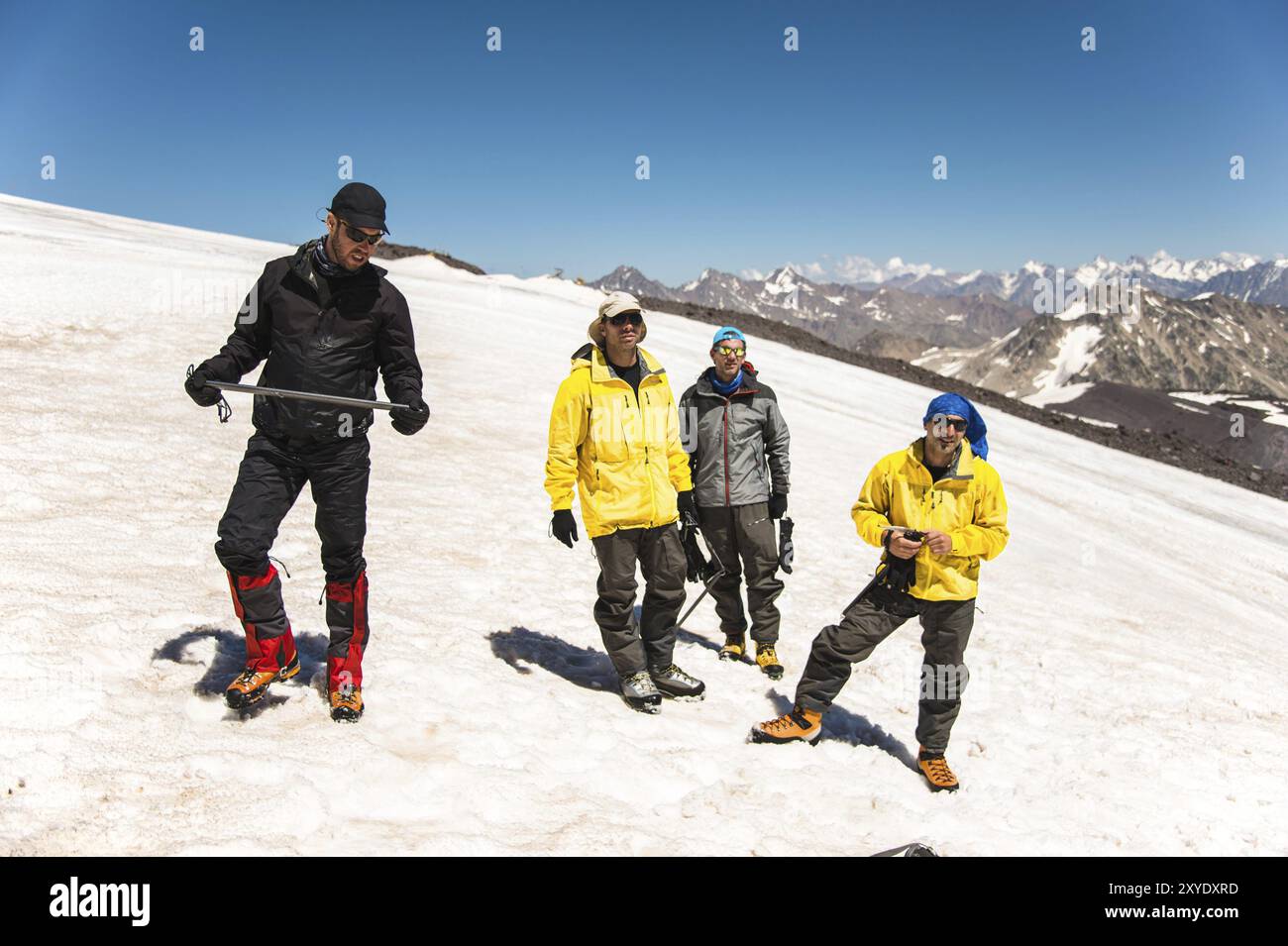 Training zum Korrigieren des Rutschens an Hanglagen oder Gletschern mit Hilfe einer Eispistole. Ein junger Reiseleiter mit Bart erklärt seiner Gruppe, wie man das richtig verlangsamt Stockfoto