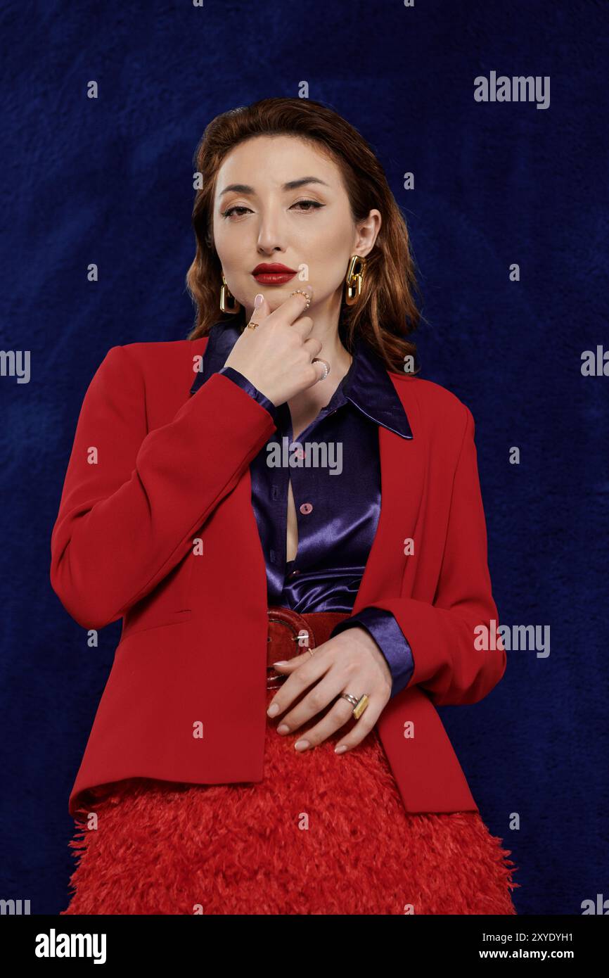 Eine attraktive asiatische Frau in einem leuchtend roten Anzug und einem Seidenhemd posiert selbstbewusst vor einem dunkelblauen Hintergrund. Stockfoto